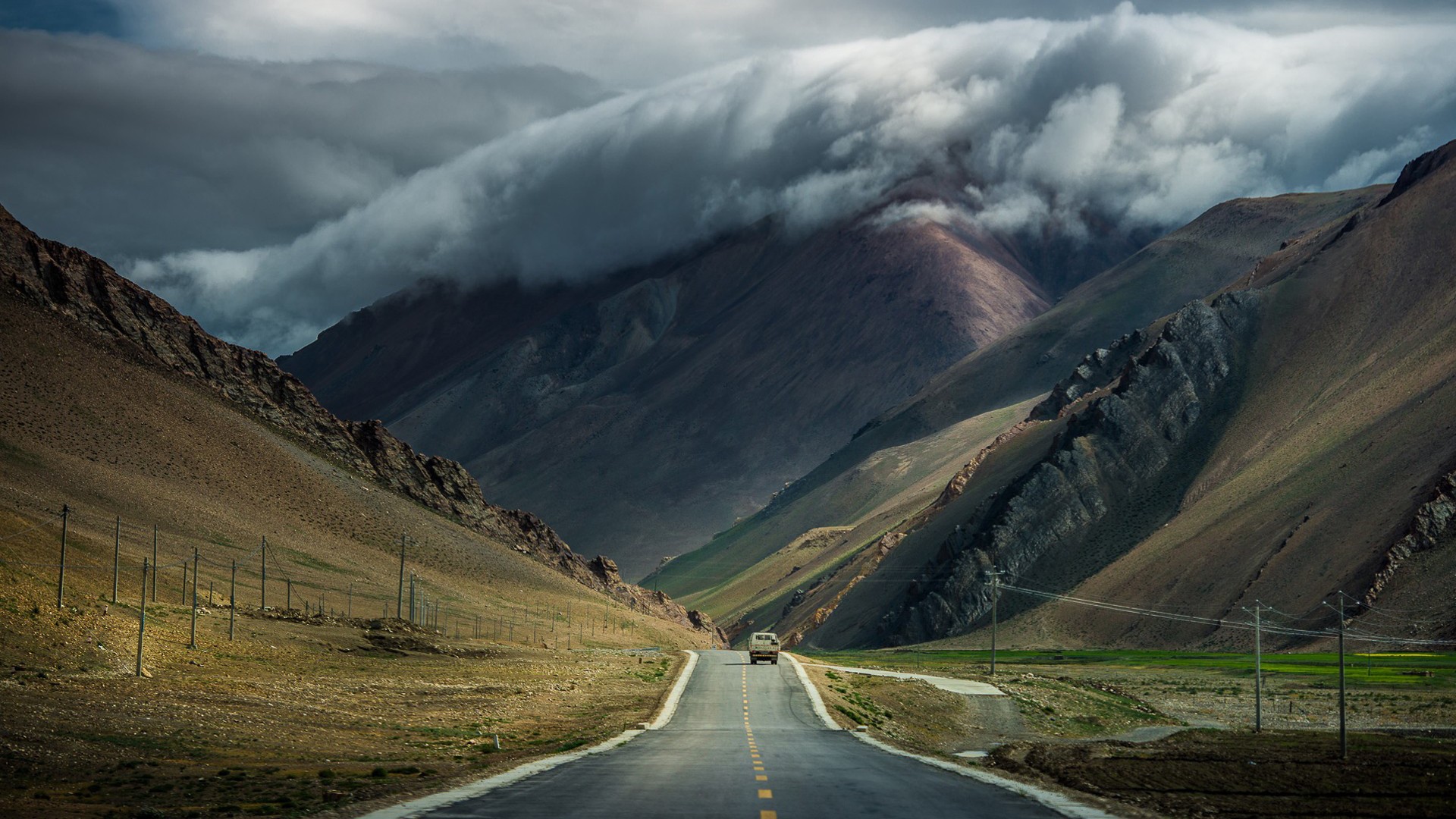A vehicle drives on a road through a mountain pass HD Wallpaper