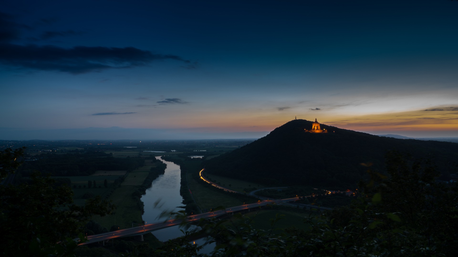 Hilltop monument illuminated at dusk with river and road below HD Wallpaper