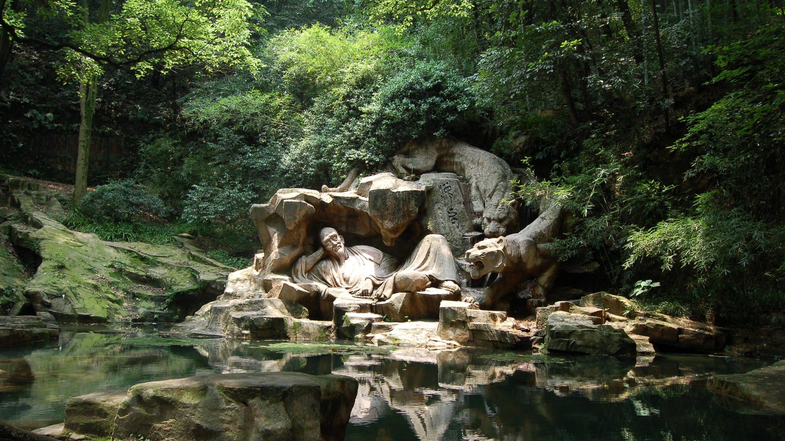 Sculpture of a man and tigers in a forest near water HD Wallpaper