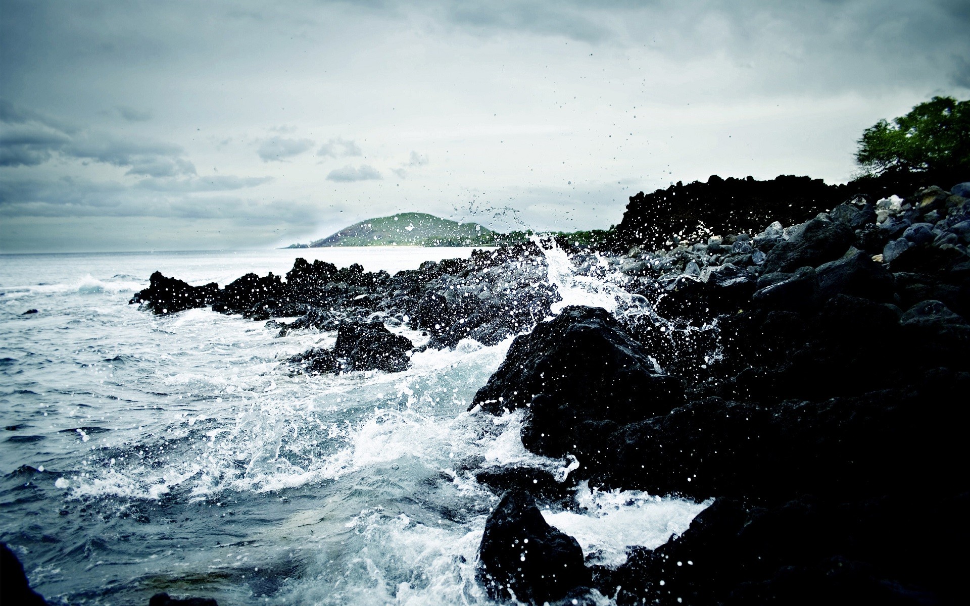 Waves crashing on dark rocks under an overcast sky HD Wallpaper
