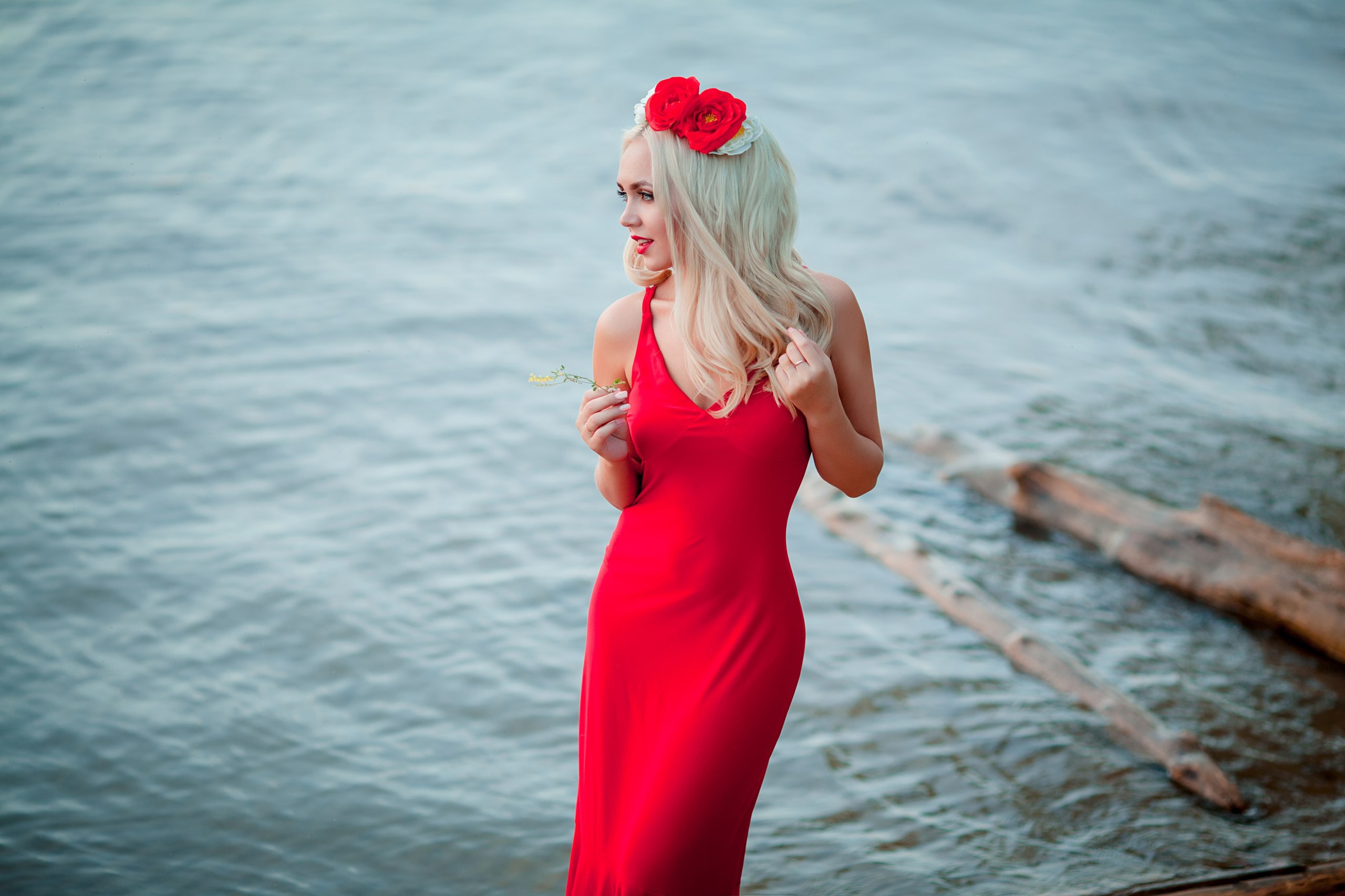 Woman in red dress with flowers in hair by water HD Wallpaper