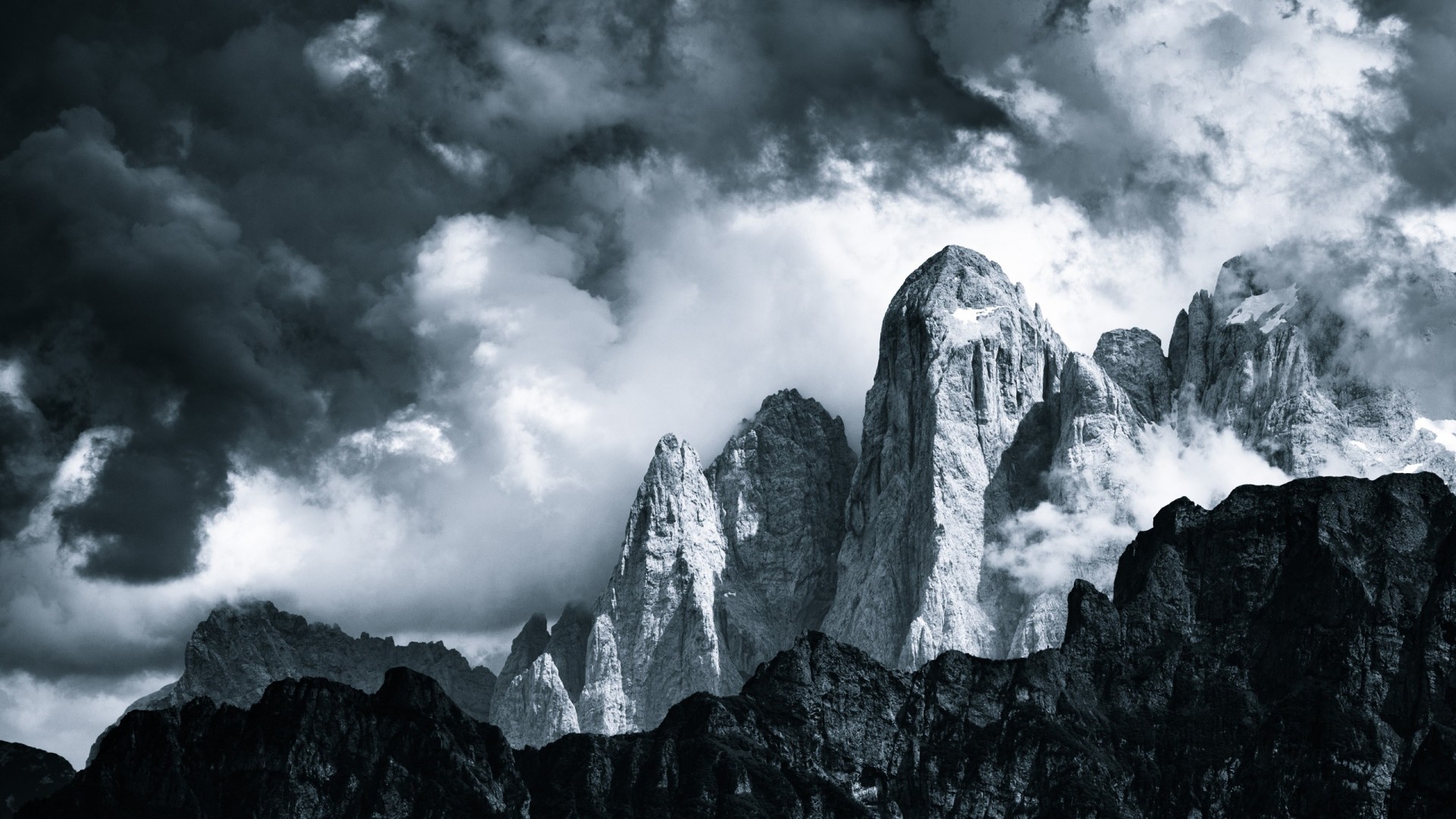 Dark clouds over jagged mountain peaks in monochrome HD Wallpaper