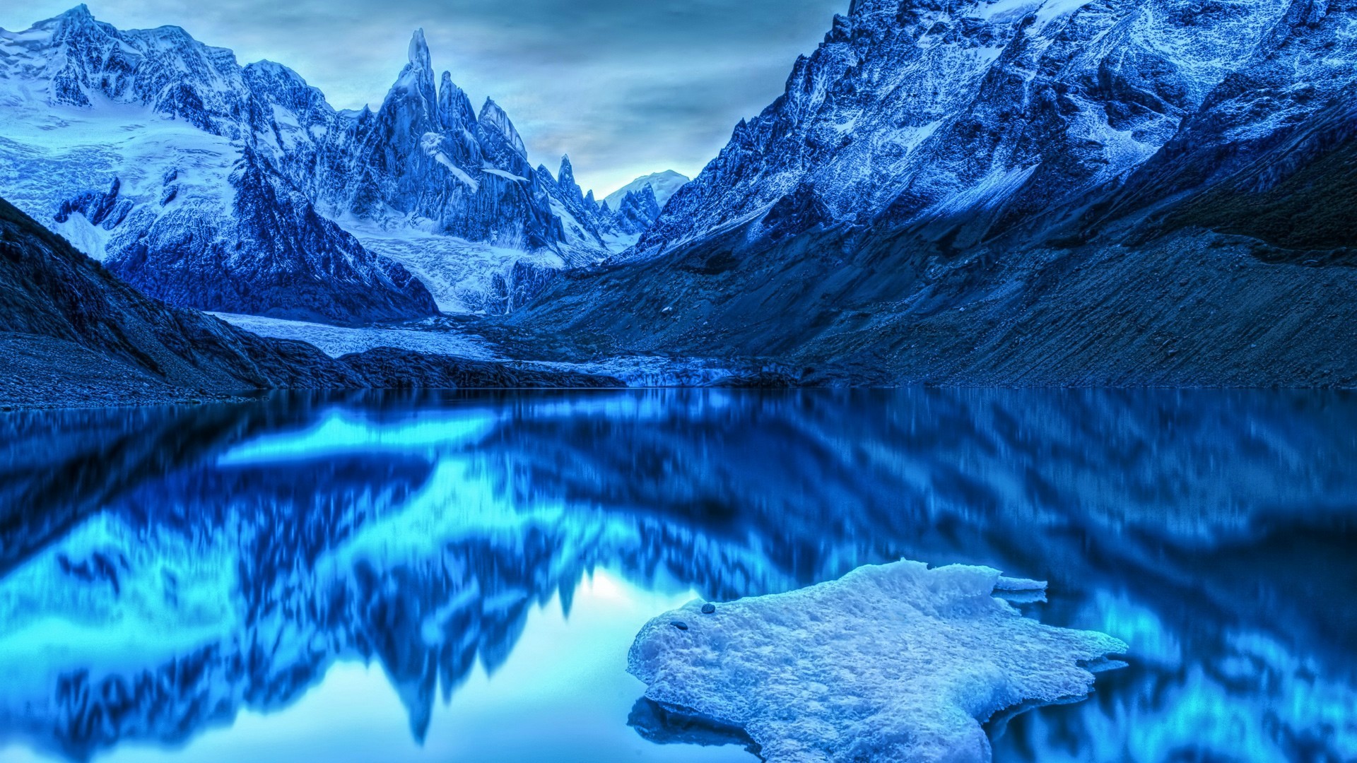 Blue glacial mountains reflected in a lake with ice floe HD Wallpaper