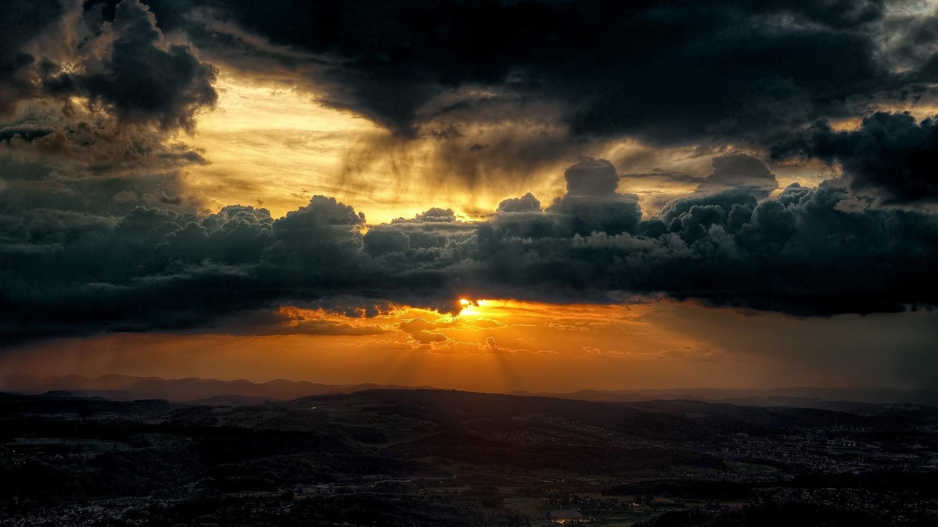 Dramatic sunset with dark storm clouds over a landscape HD Wallpaper
