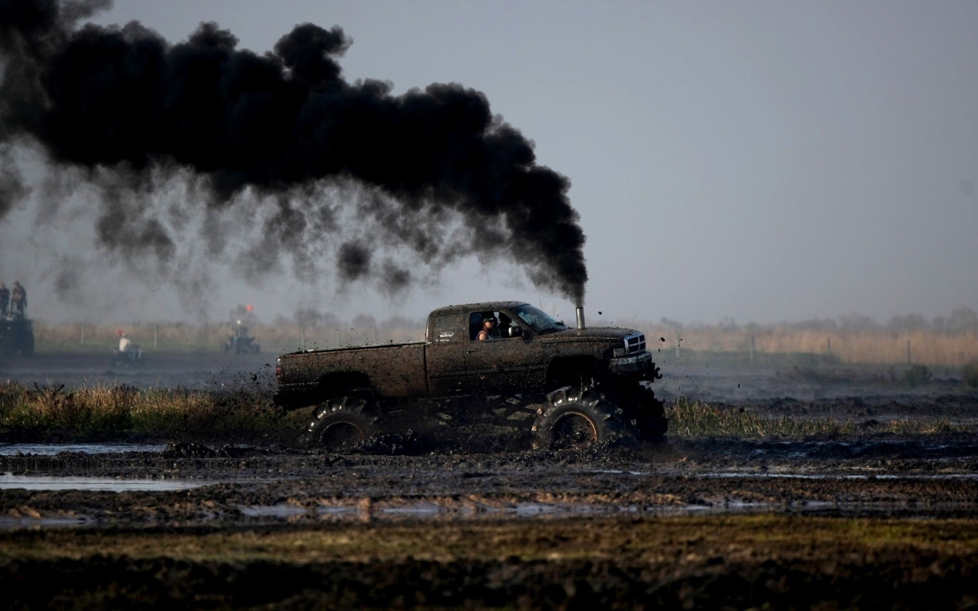 Monster truck emitting black smoke in a mud pit HD Wallpaper
