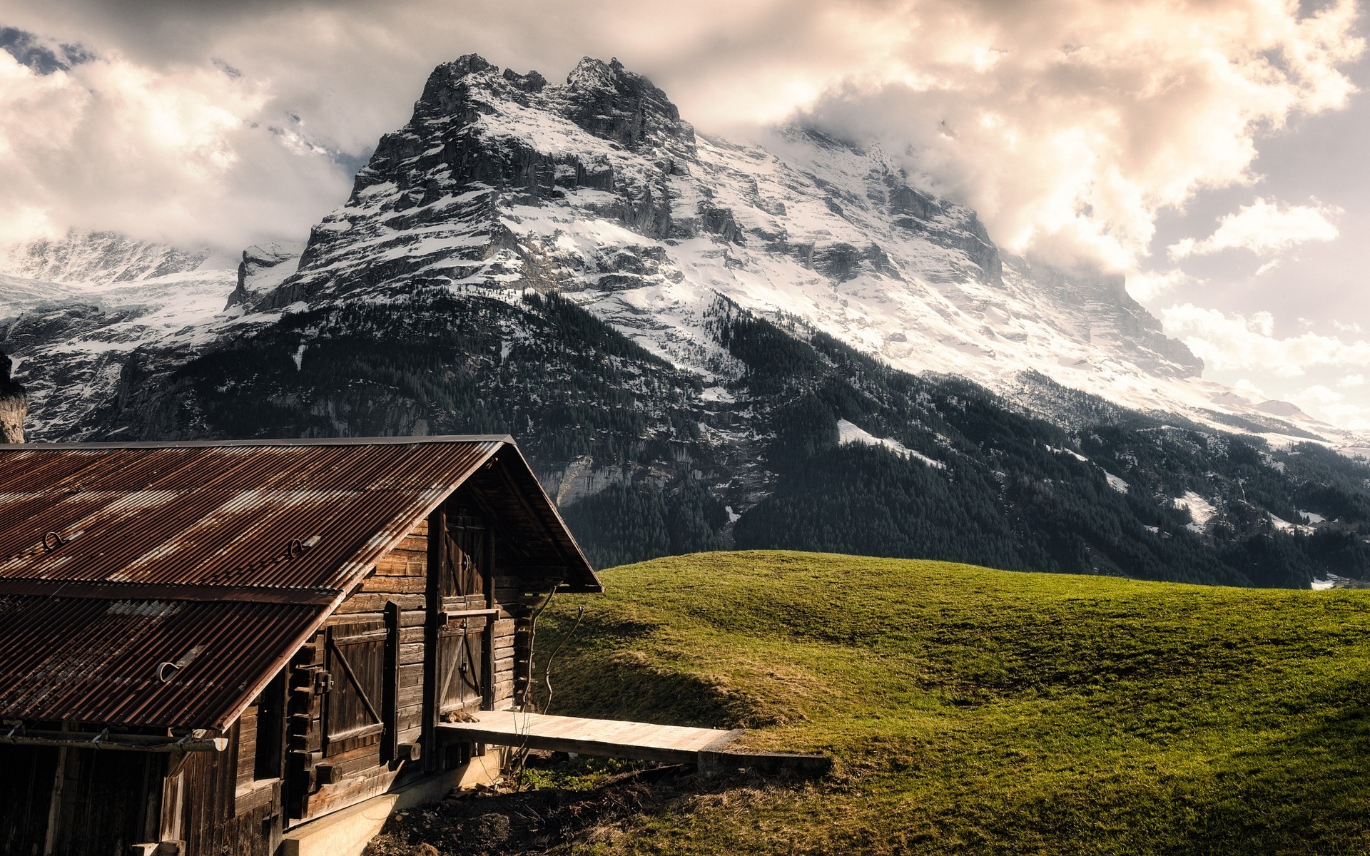 Wooden cabin in front of a snowy mountain peak in Switzerland HD Wallpaper