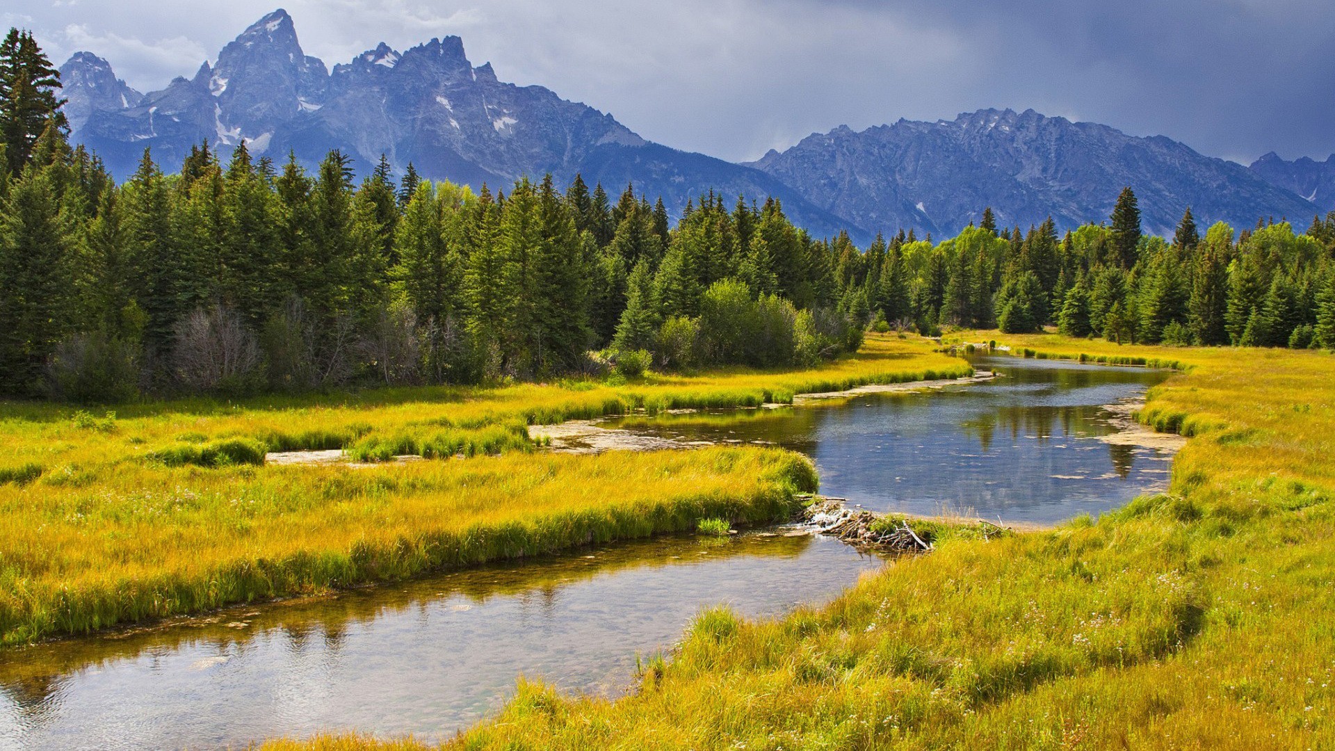 River flowing through a meadow with mountains in the background HD Wallpaper