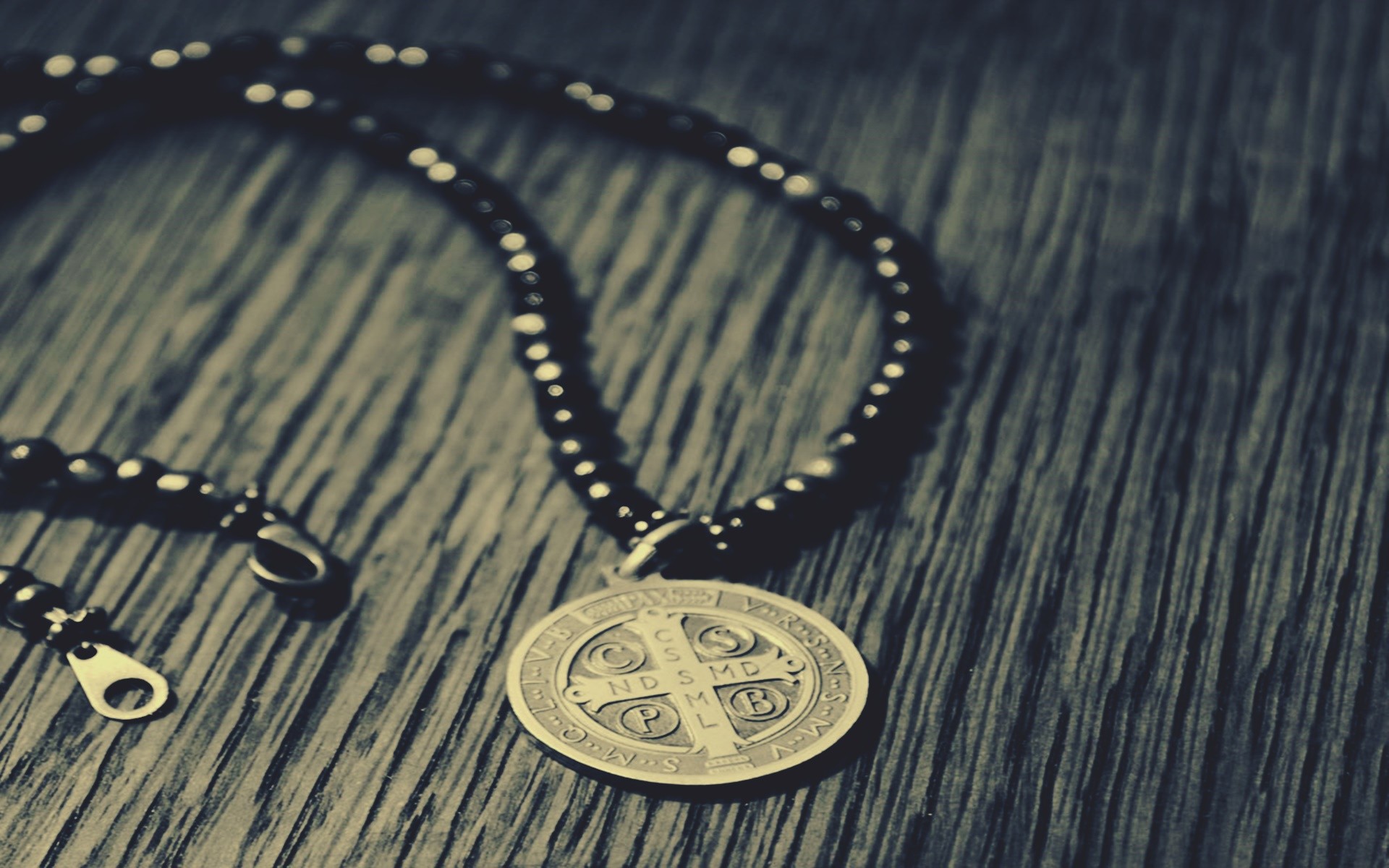 Saint Benedict Medal necklace on a wooden surface HD Wallpaper