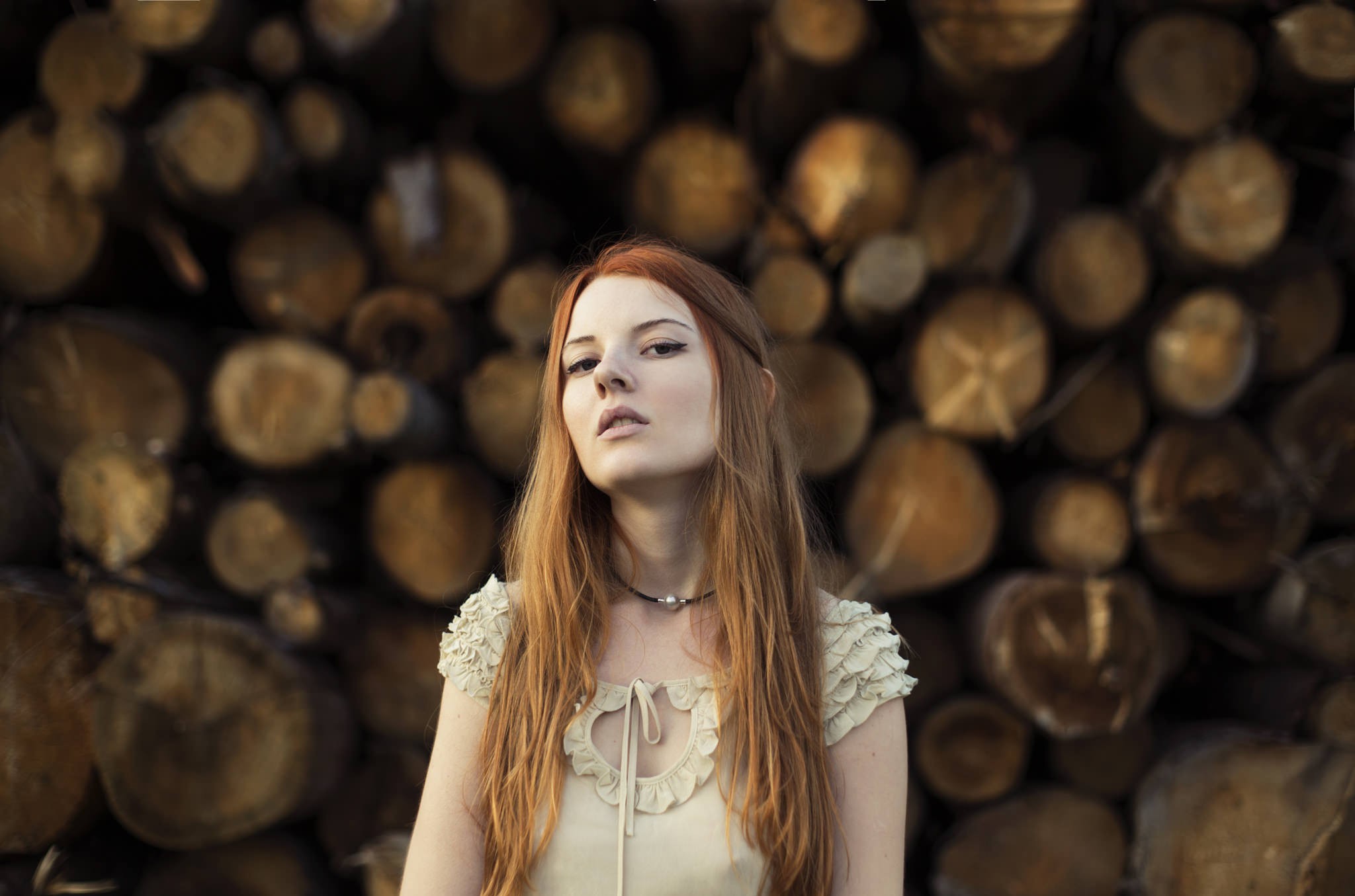 Redhead woman in a light-colored dress standing in front of logs HD Wallpaper