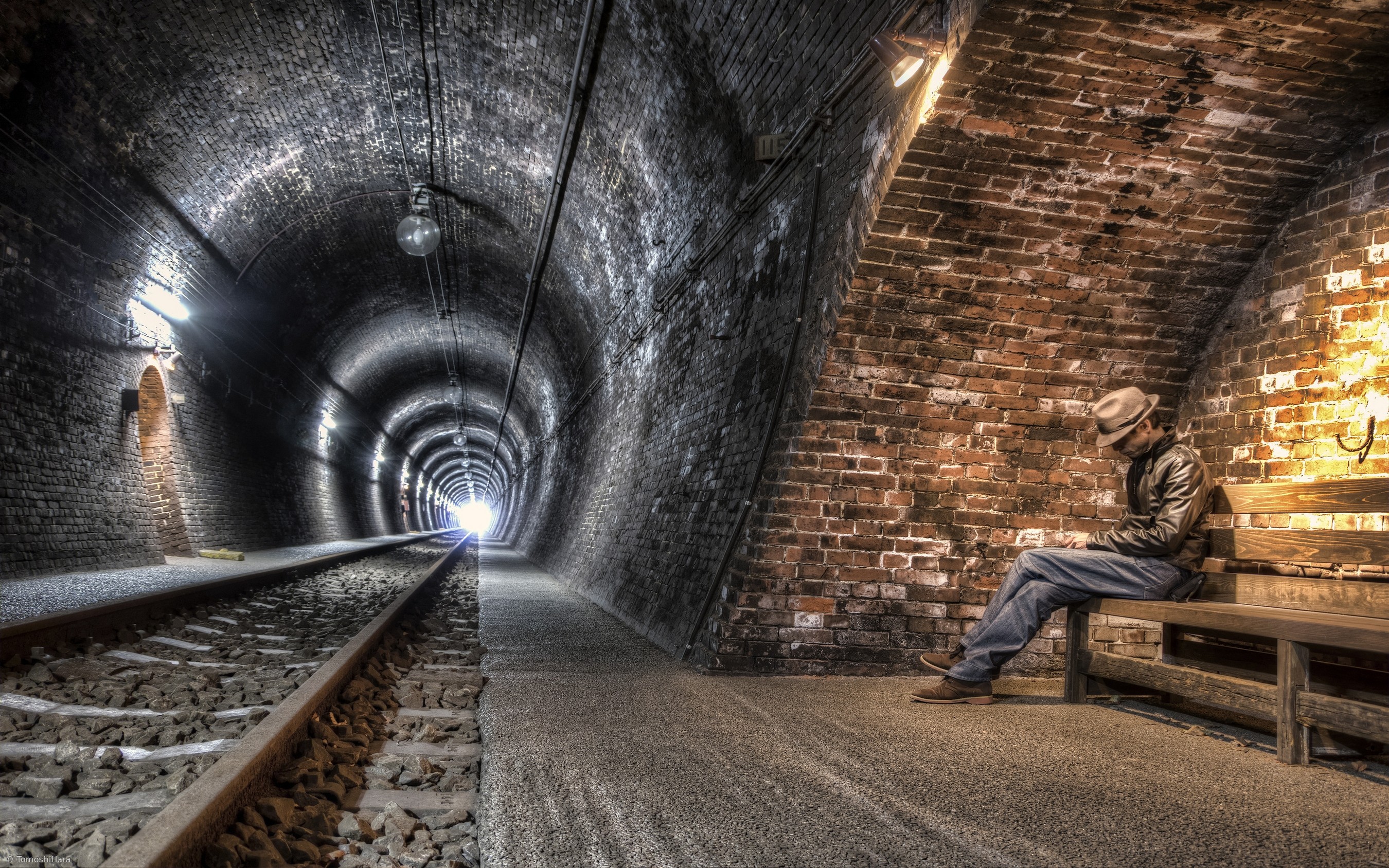 Man sitting on a bench in a brick tunnel HD Wallpaper