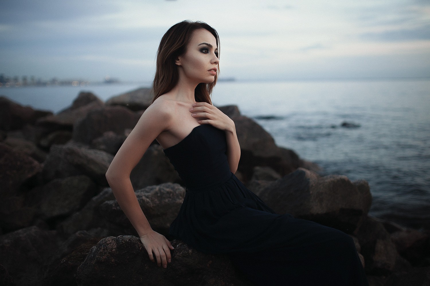 Woman in black dress sitting on rocks by the sea HD Wallpaper