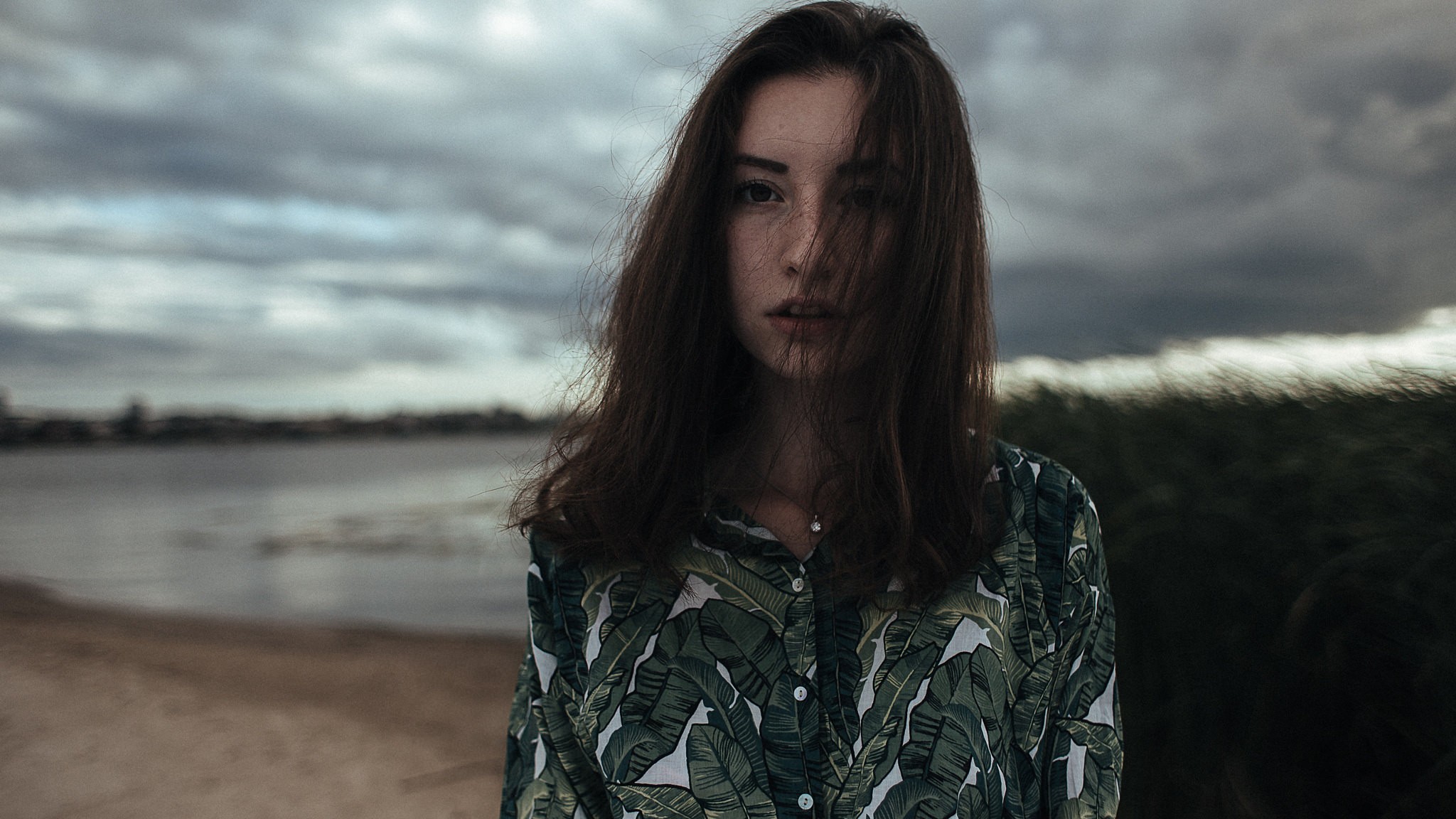 Woman with dark hair in a patterned shirt by the water HD Wallpaper
