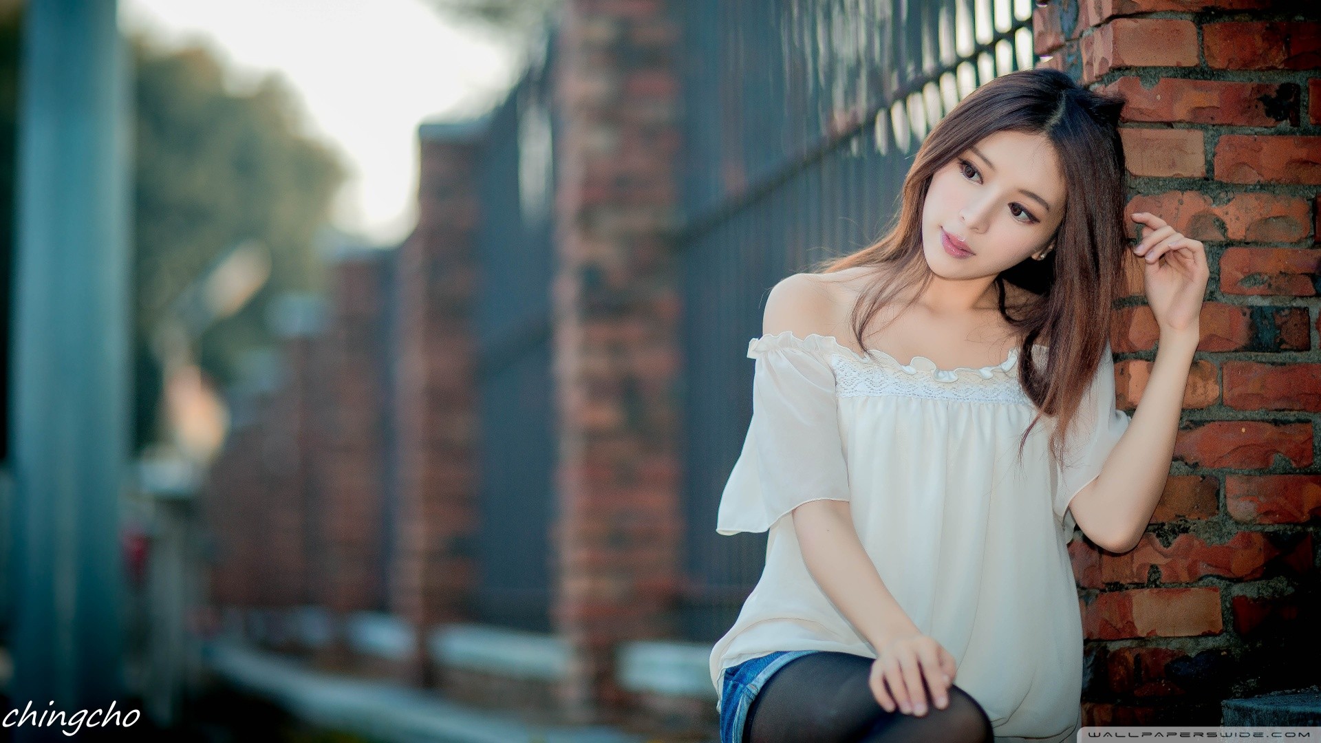 Asian woman leaning against a brick wall HD Wallpaper
