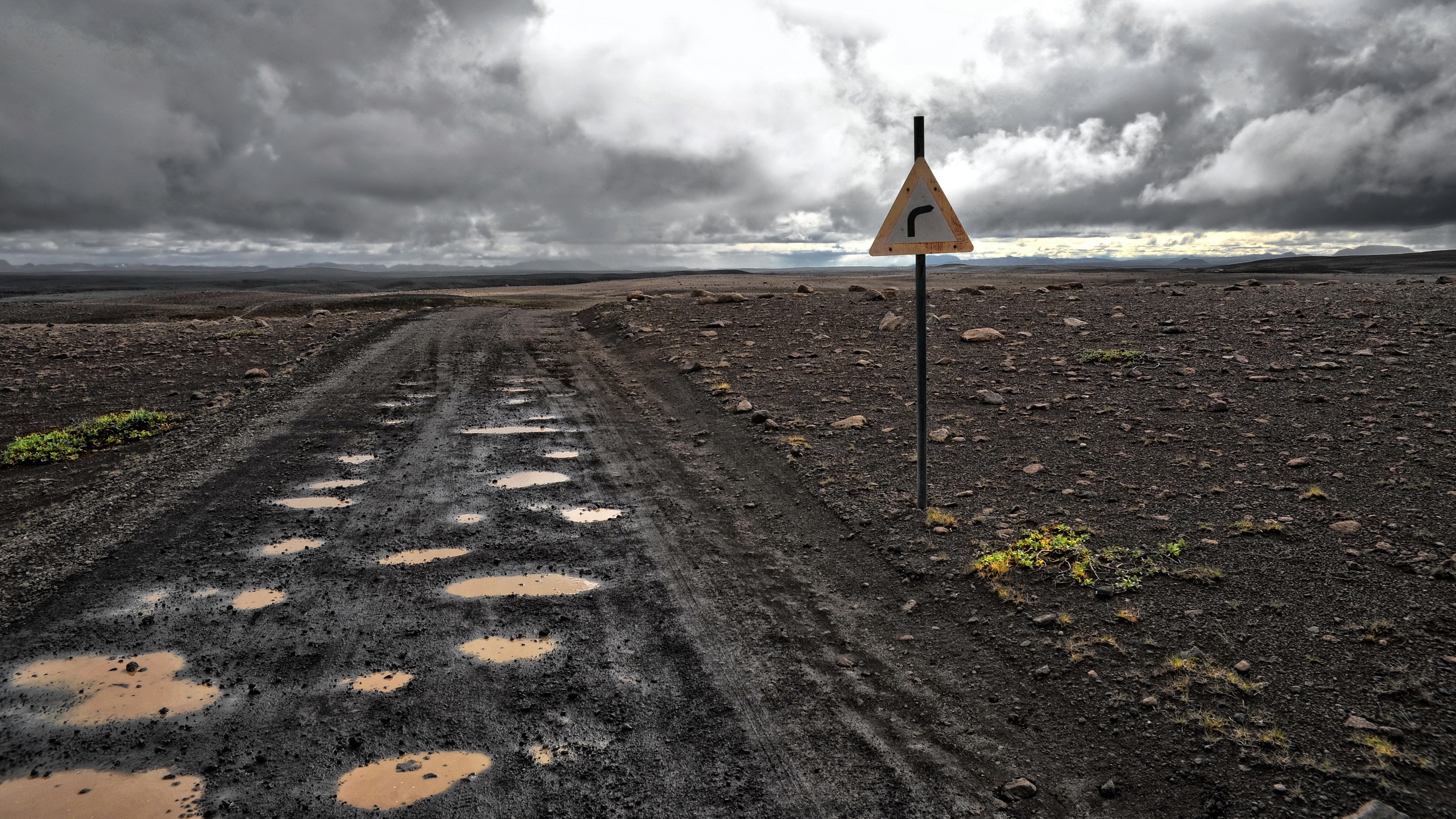 Muddy road with a traffic sign in a desolate landscape HD Wallpaper