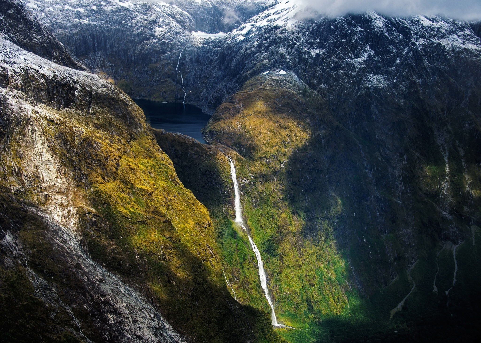 Waterfall cascading down a mossy mountain into a dark lake HD Wallpaper