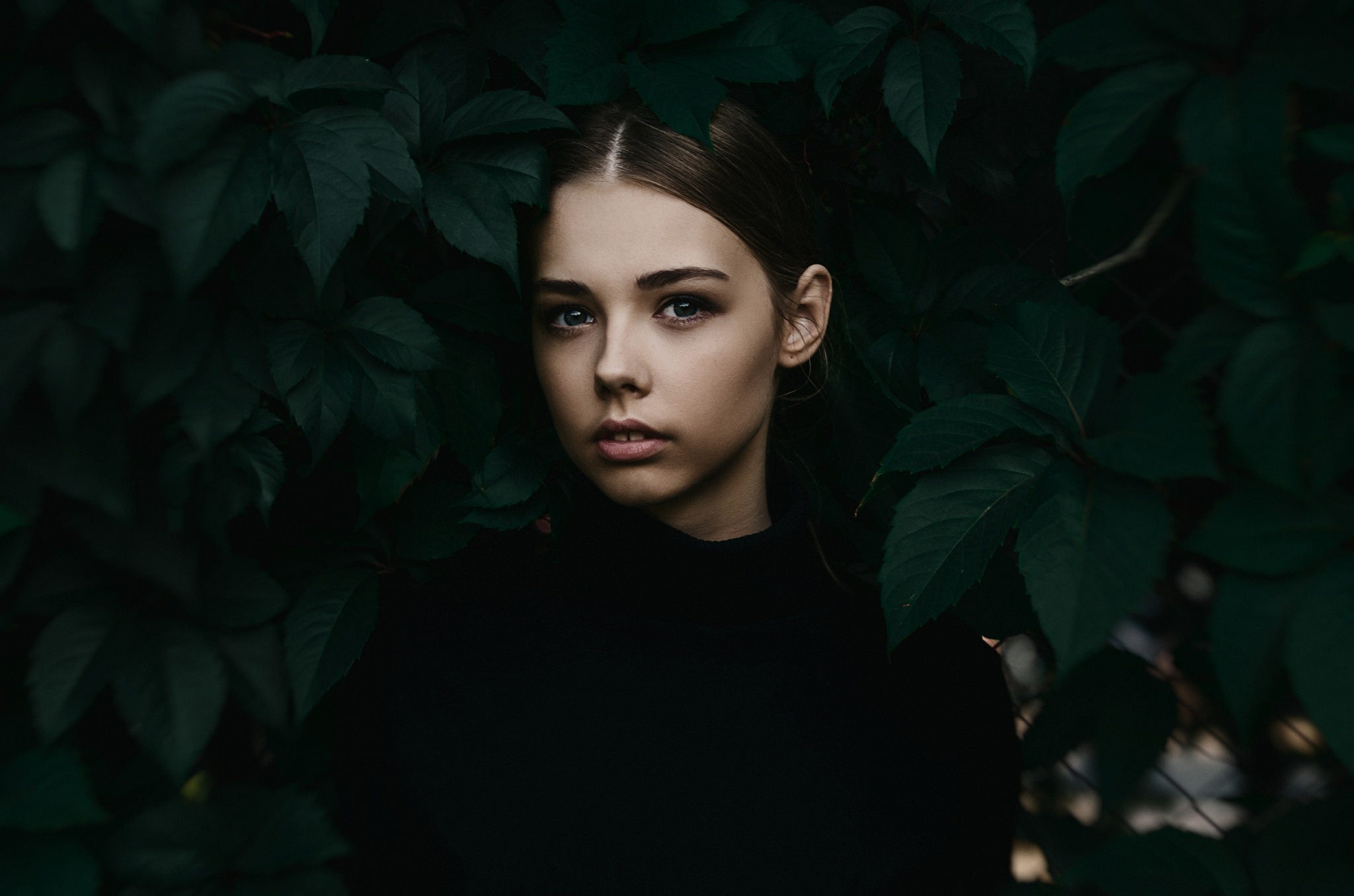 Portrait of a young woman among dark green leaves HD Wallpaper