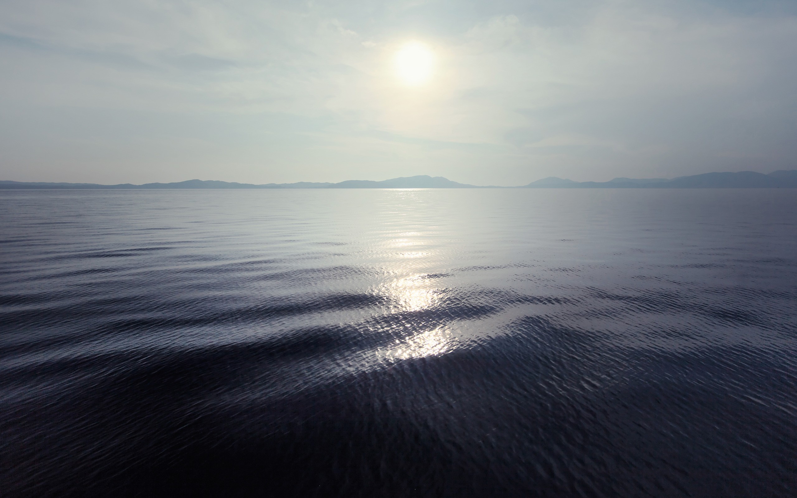 Sunlight reflecting on the sea with distant mountains HD Wallpaper