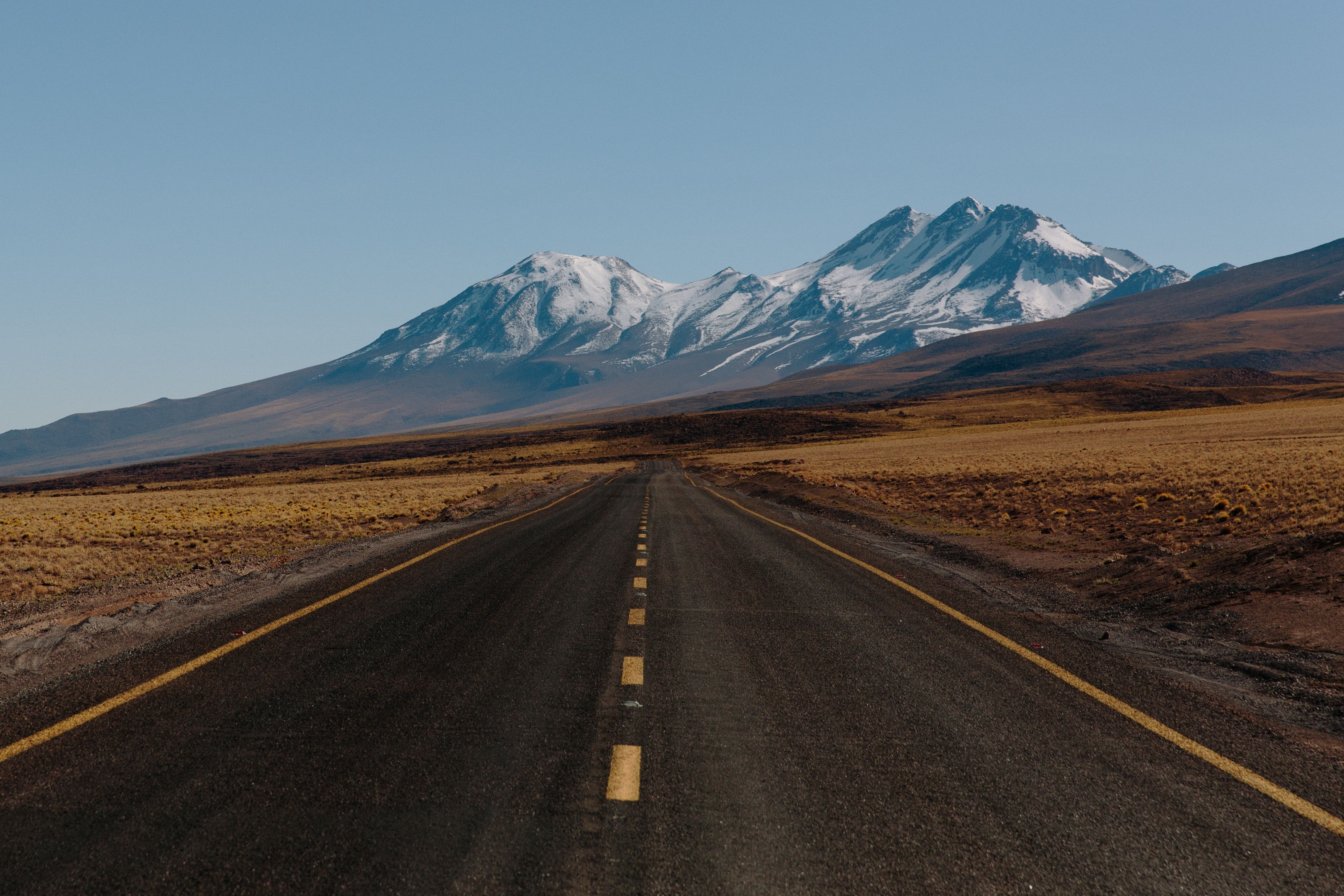 Road leading to snow-capped mountains under a clear sky HD Wallpaper