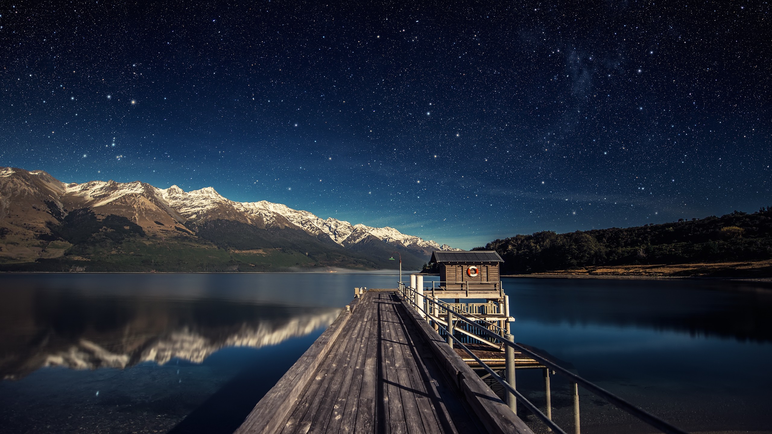 Wooden pier under a starry night sky with mountains HD Wallpaper