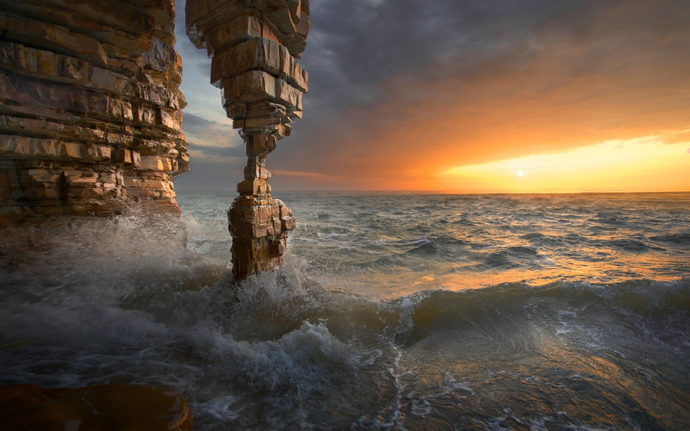 Sunset over the sea with rock formations and waves HD Wallpaper
