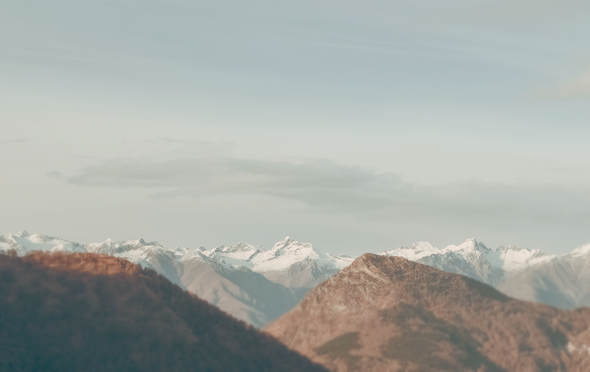 Snow-capped mountains and forested hills under a pale sky HD Wallpaper