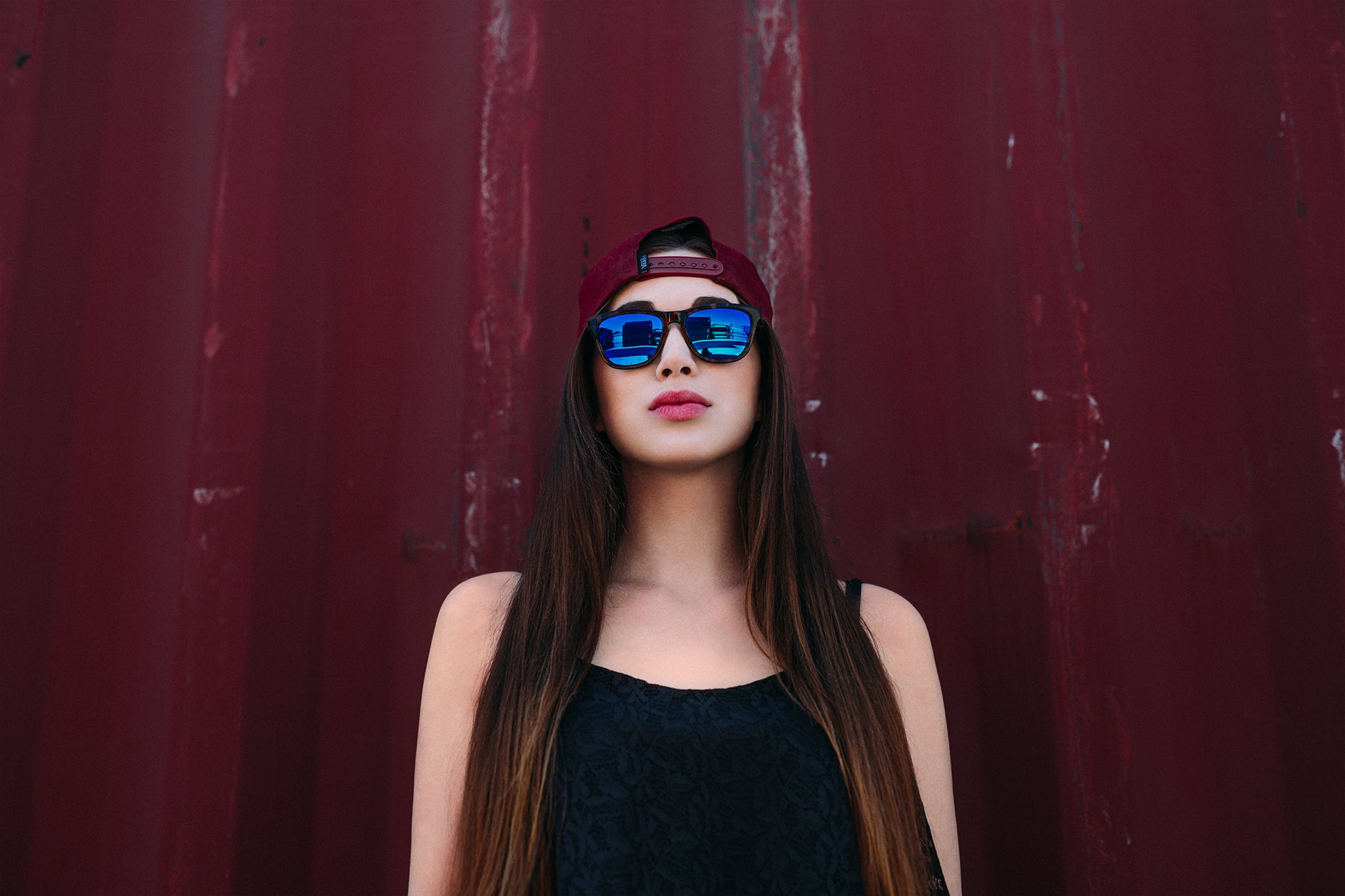 Woman wearing sunglasses and a cap against a red wall HD Wallpaper