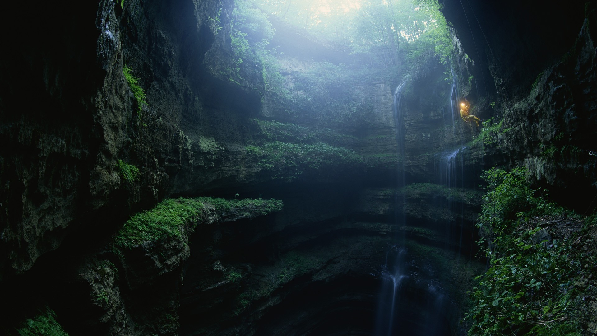 Person rappelling down a waterfall in a cave HD Wallpaper