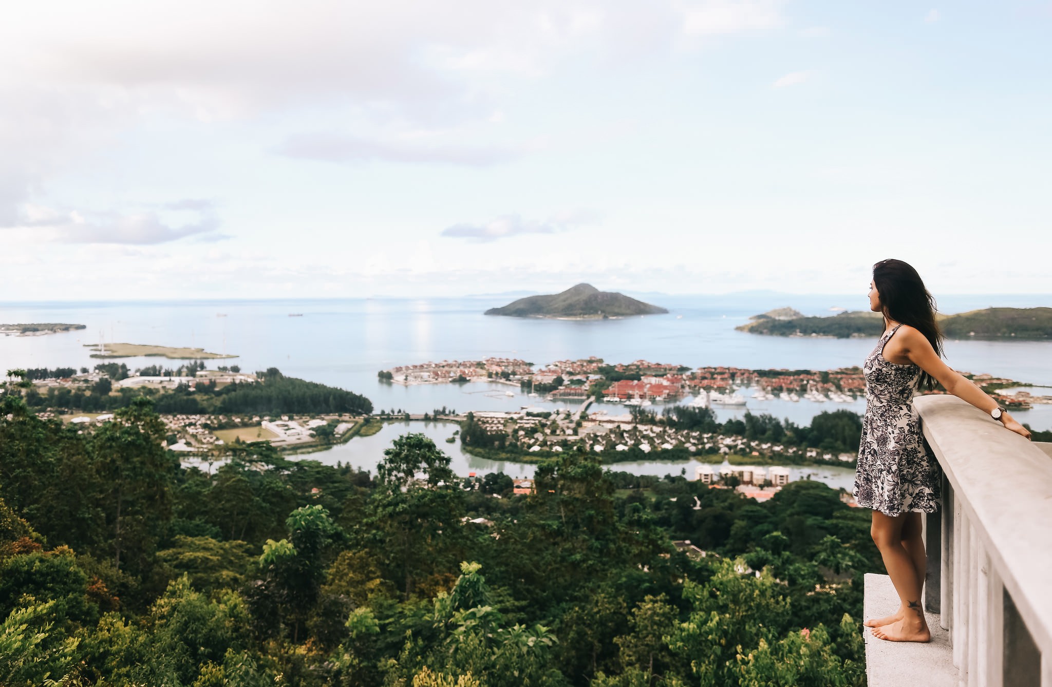 Woman looking at a coastal town from a viewpoint HD Wallpaper