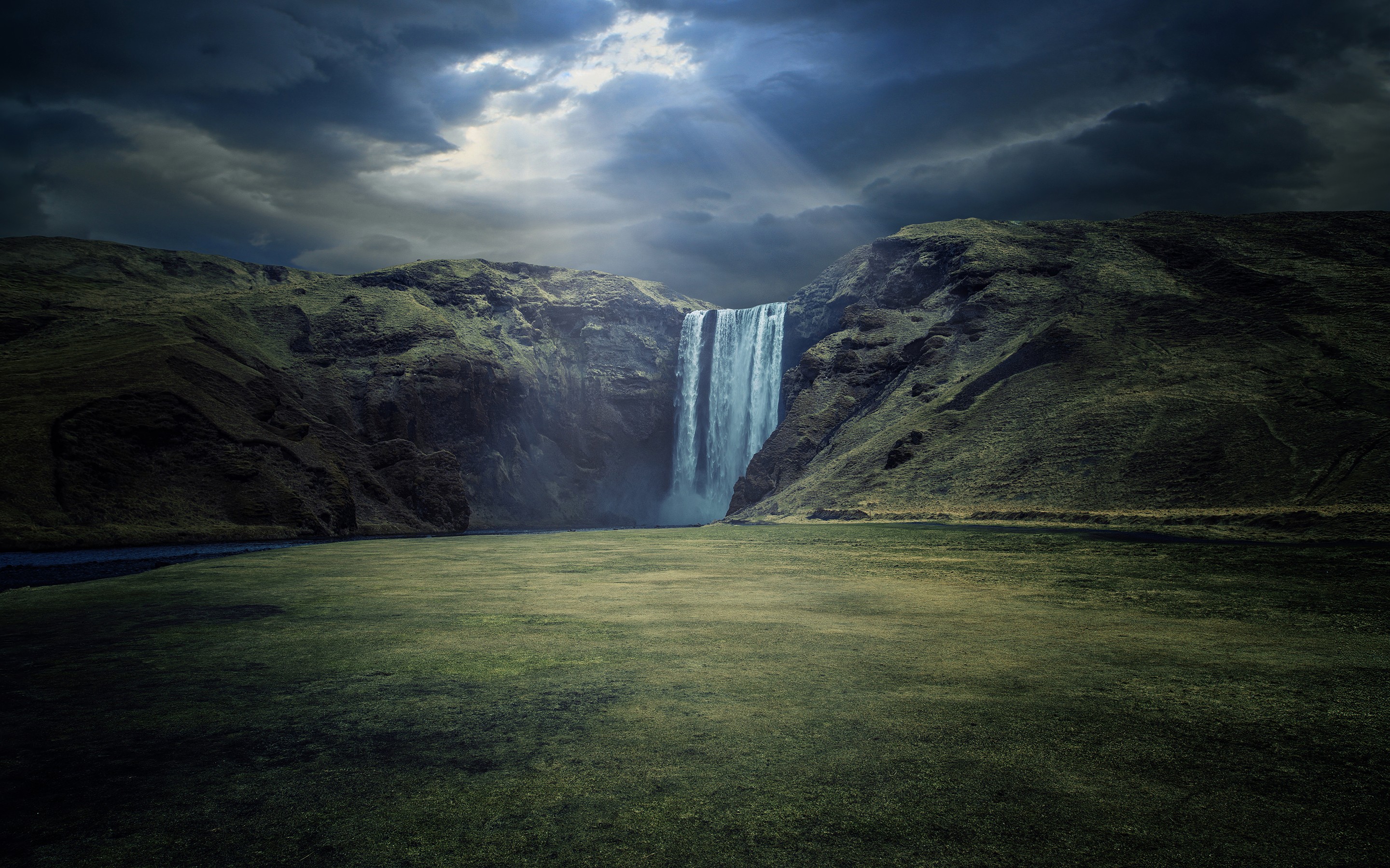 Dramatic waterfall under stormy skies in a green landscape HD Wallpaper