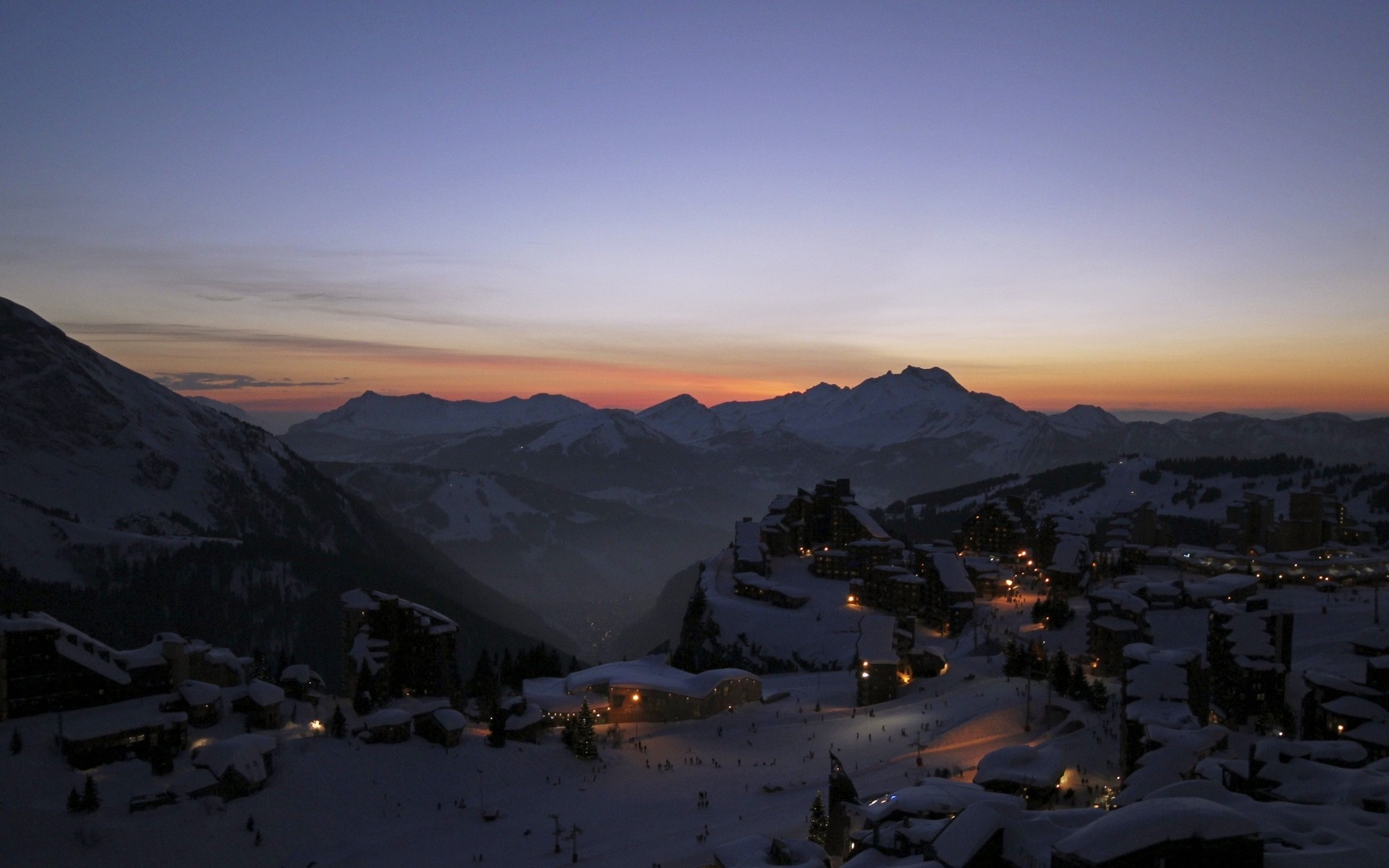 Snowy mountain village at dusk with illuminated buildings HD Wallpaper