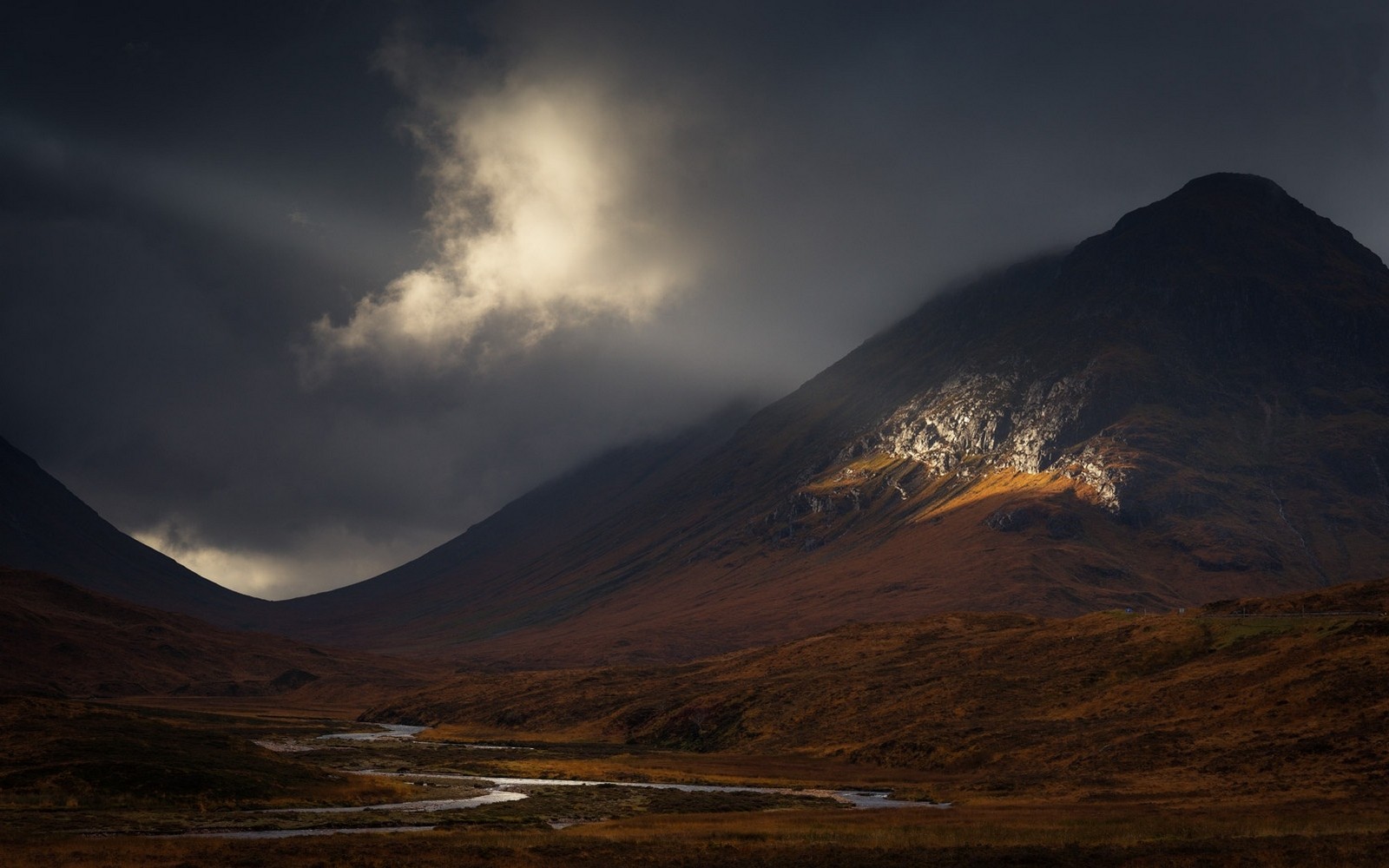 Sunbeams illuminate mountains and a river in a dark landscape HD Wallpaper