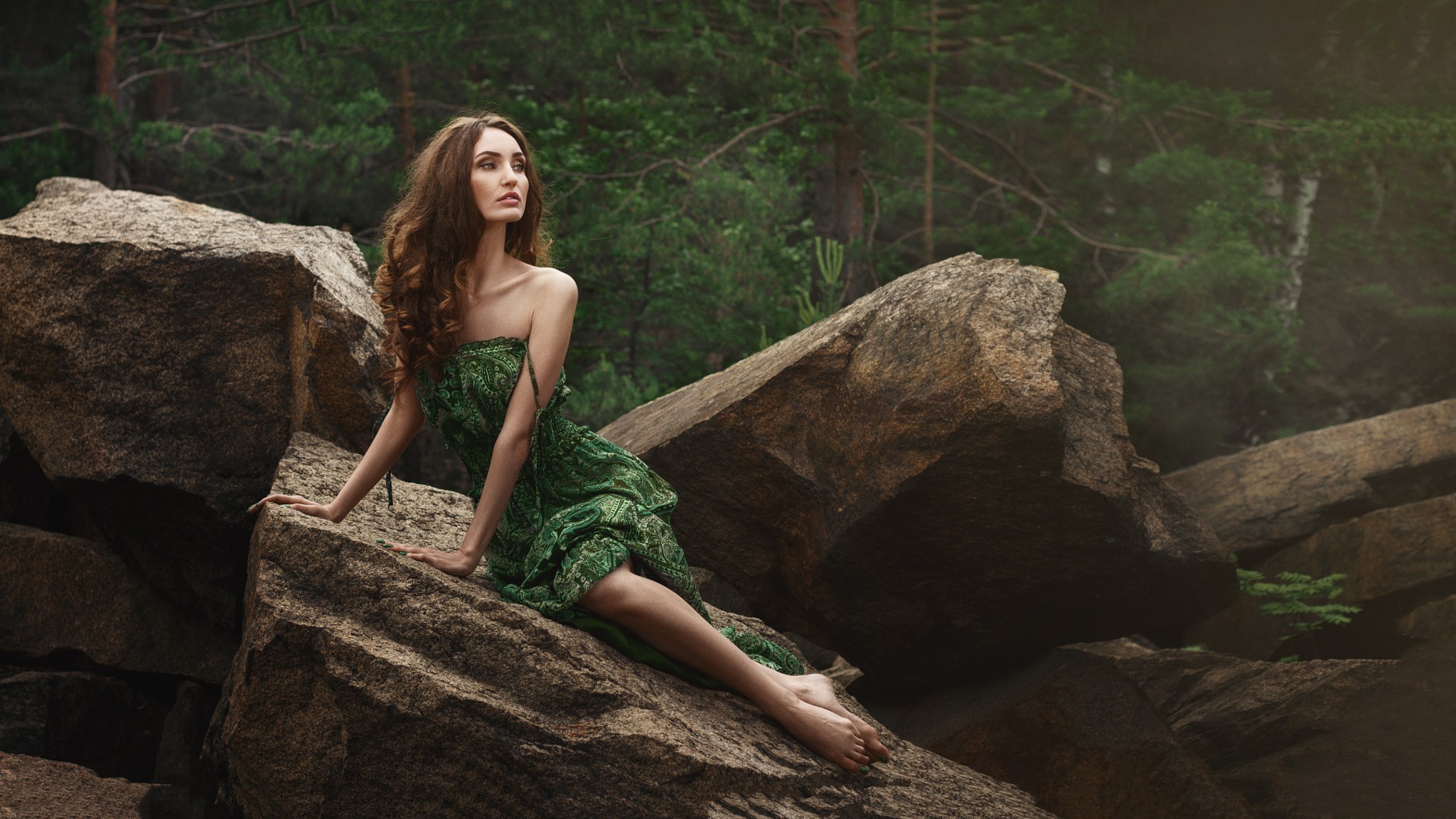 Woman in green dress sitting on rocks in forest HD Wallpaper