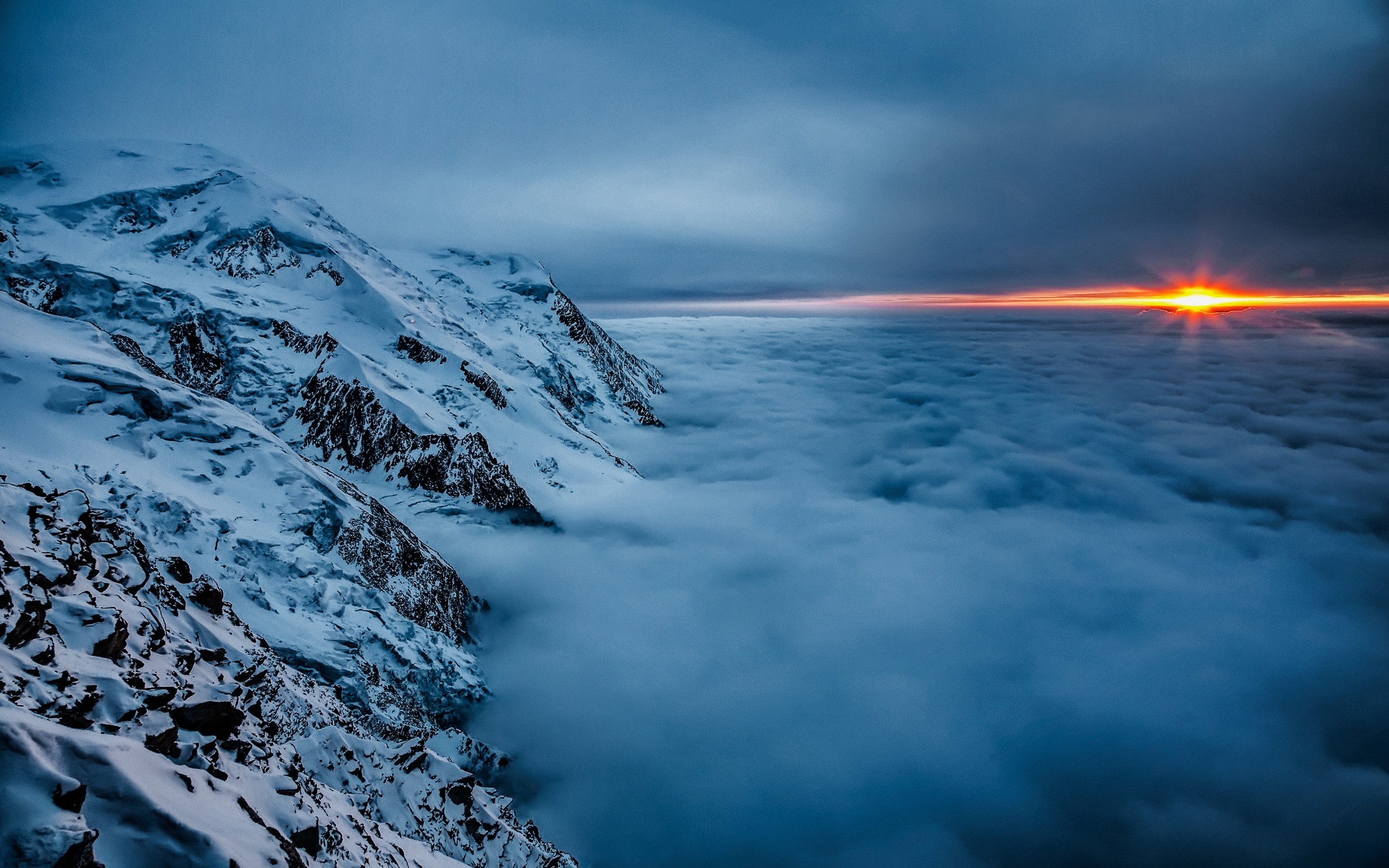 Snowy mountains above clouds at sunset HD Wallpaper