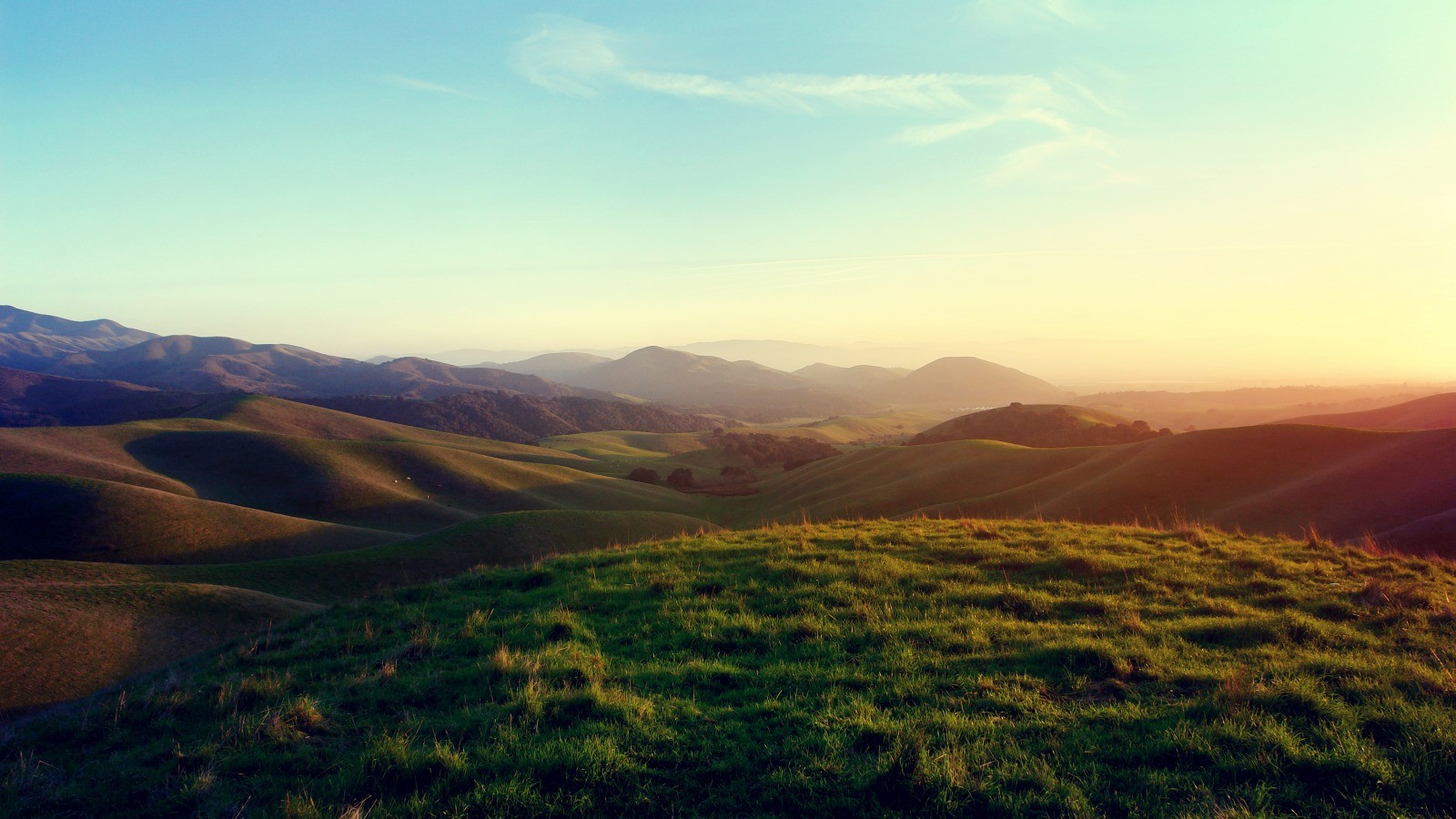 Rolling green hills and mountains at sunset HD Wallpaper