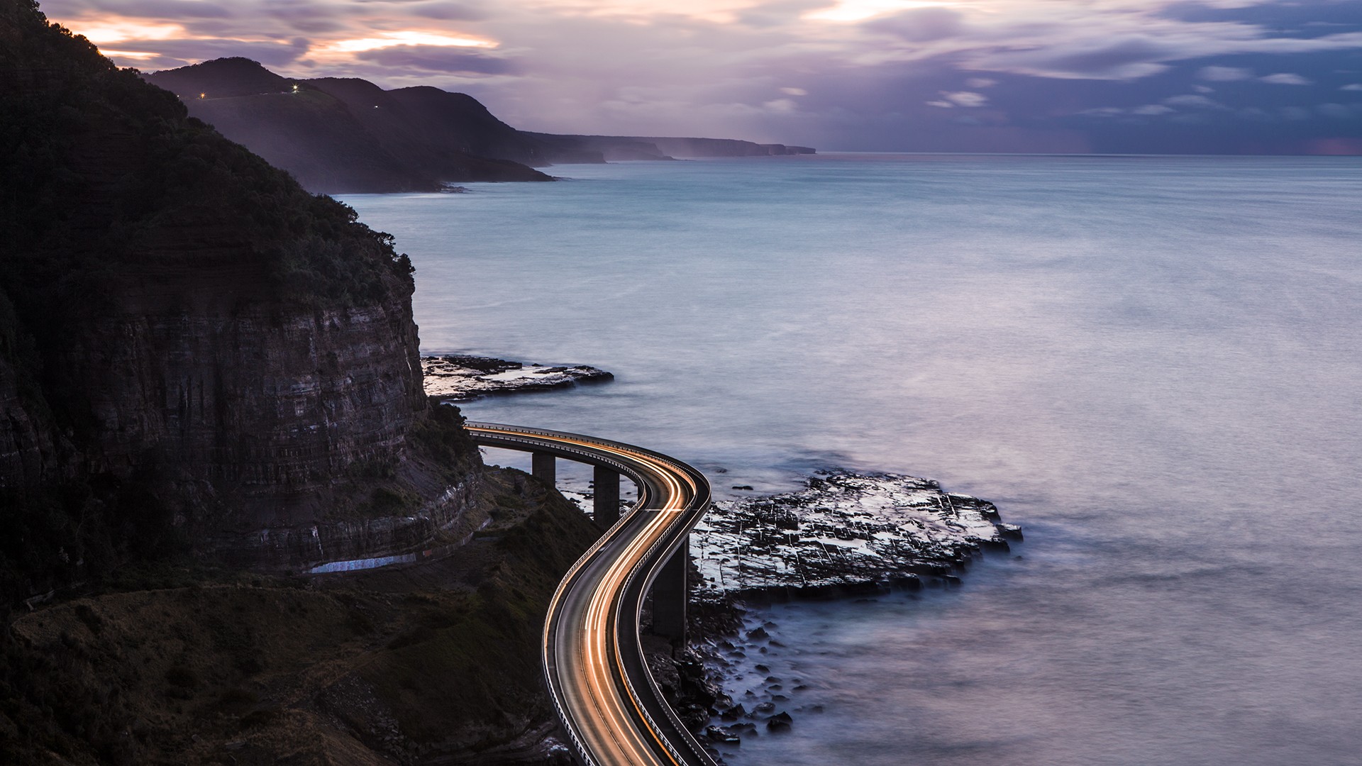 Long exposure of a coastal road with light trails at sunset HD Wallpaper