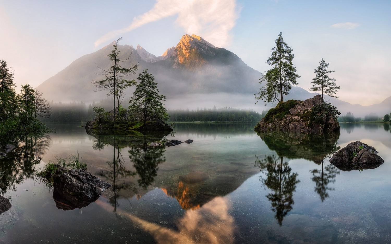 Misty mountains reflected in a calm lake with trees HD Wallpaper