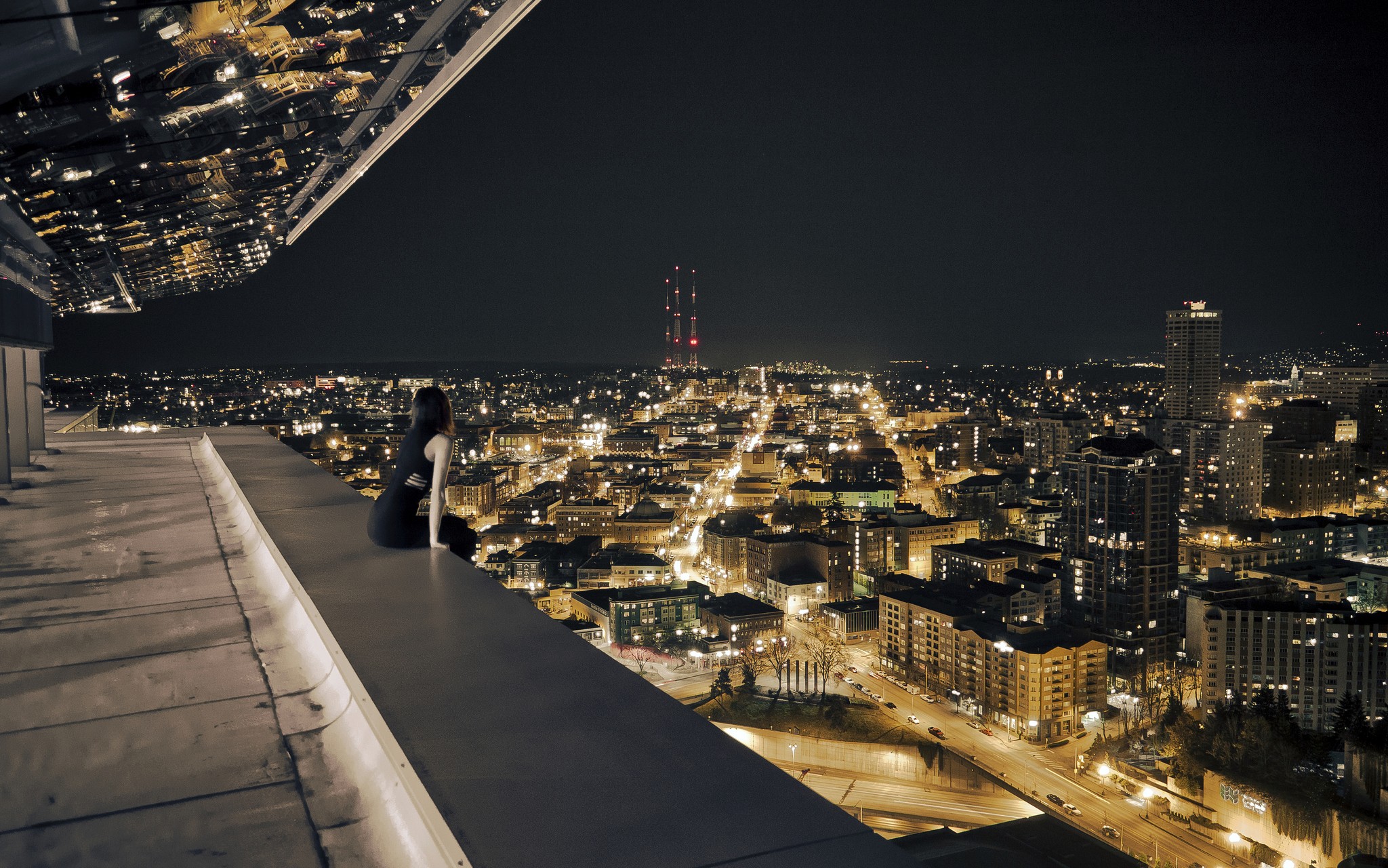Woman sitting on a rooftop overlooking a city at night HD Wallpaper