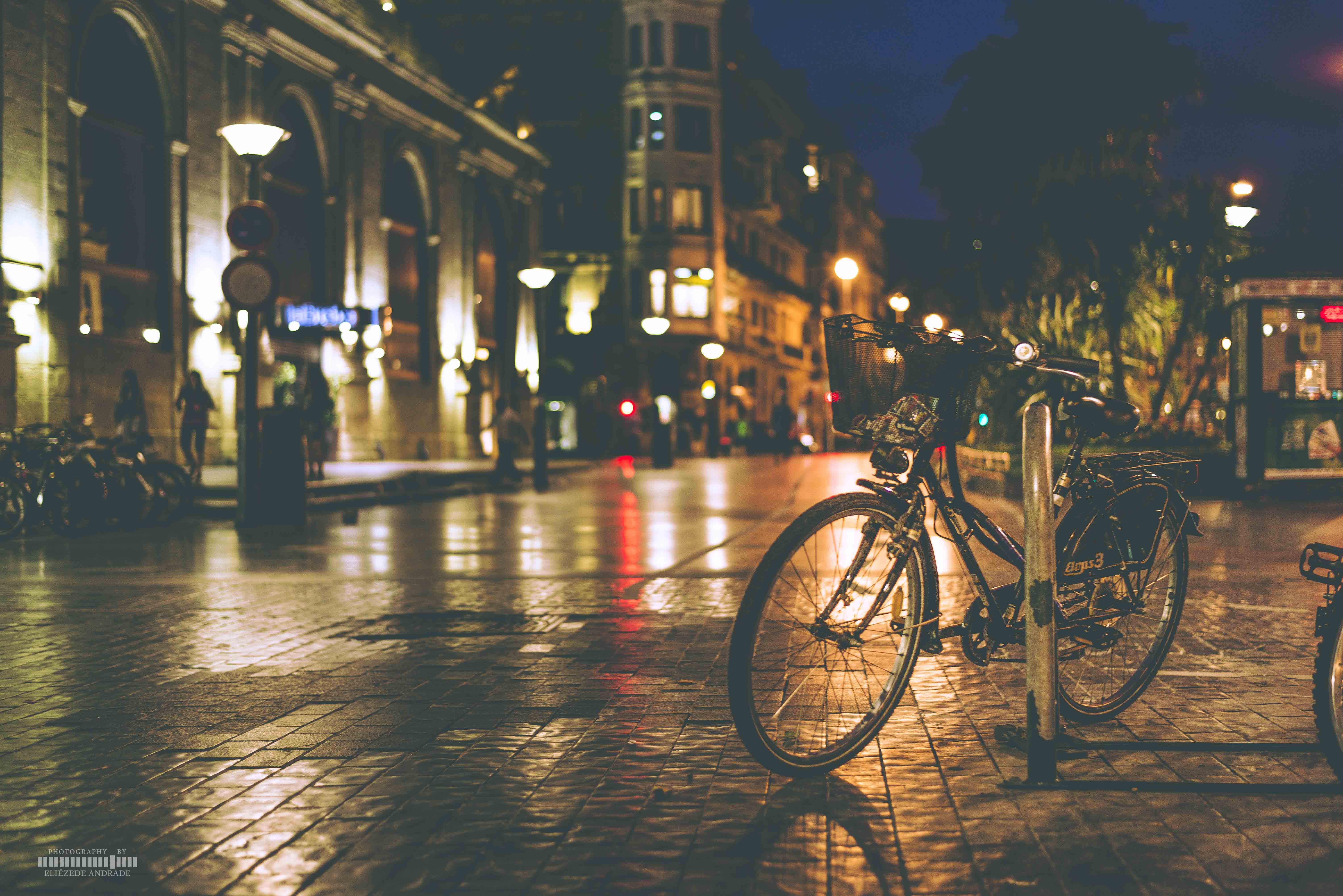 Bicycle parked on a wet cobblestone street at night HD Wallpaper