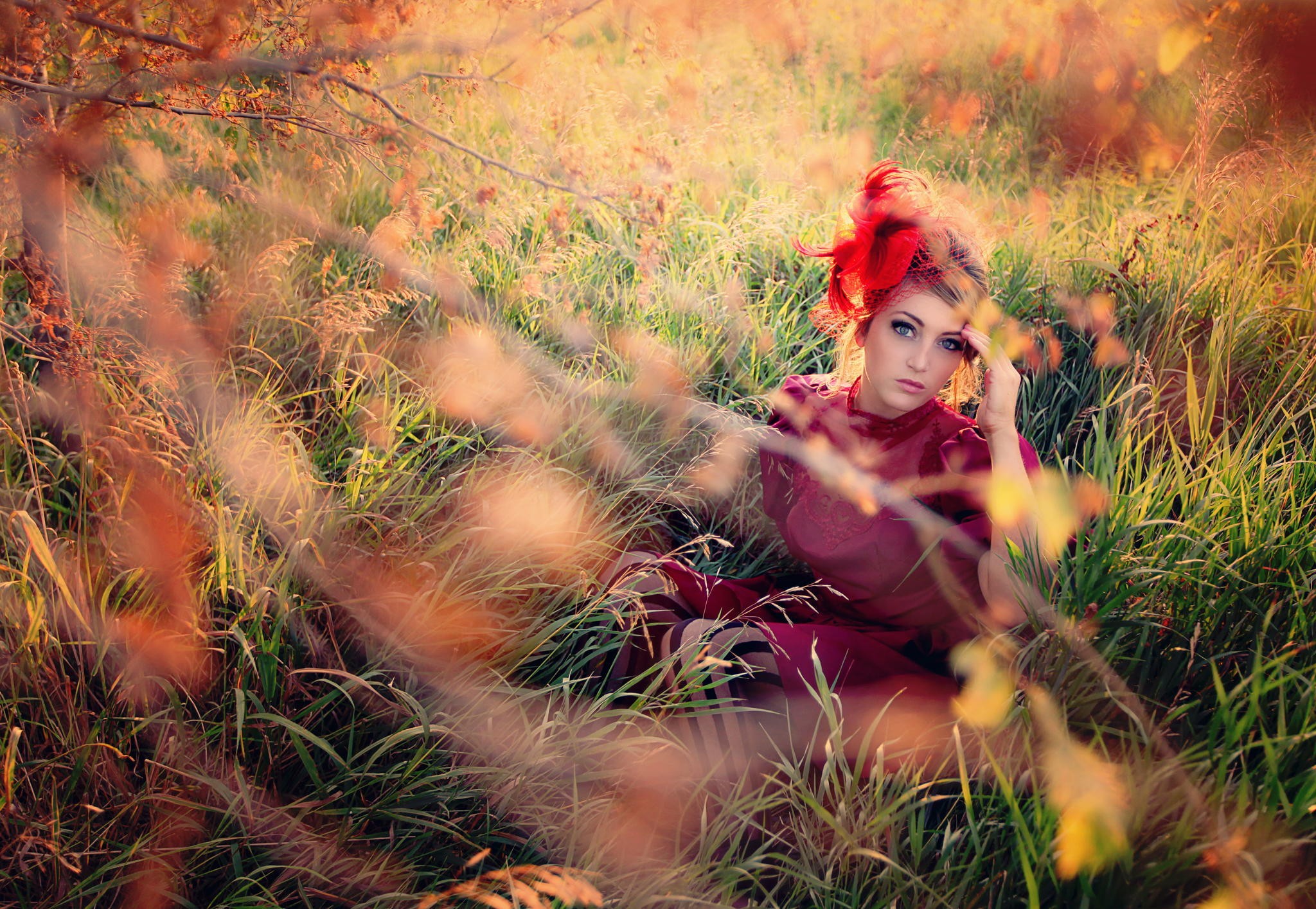 Woman in red dress with red fascinator sitting in grass HD Wallpaper