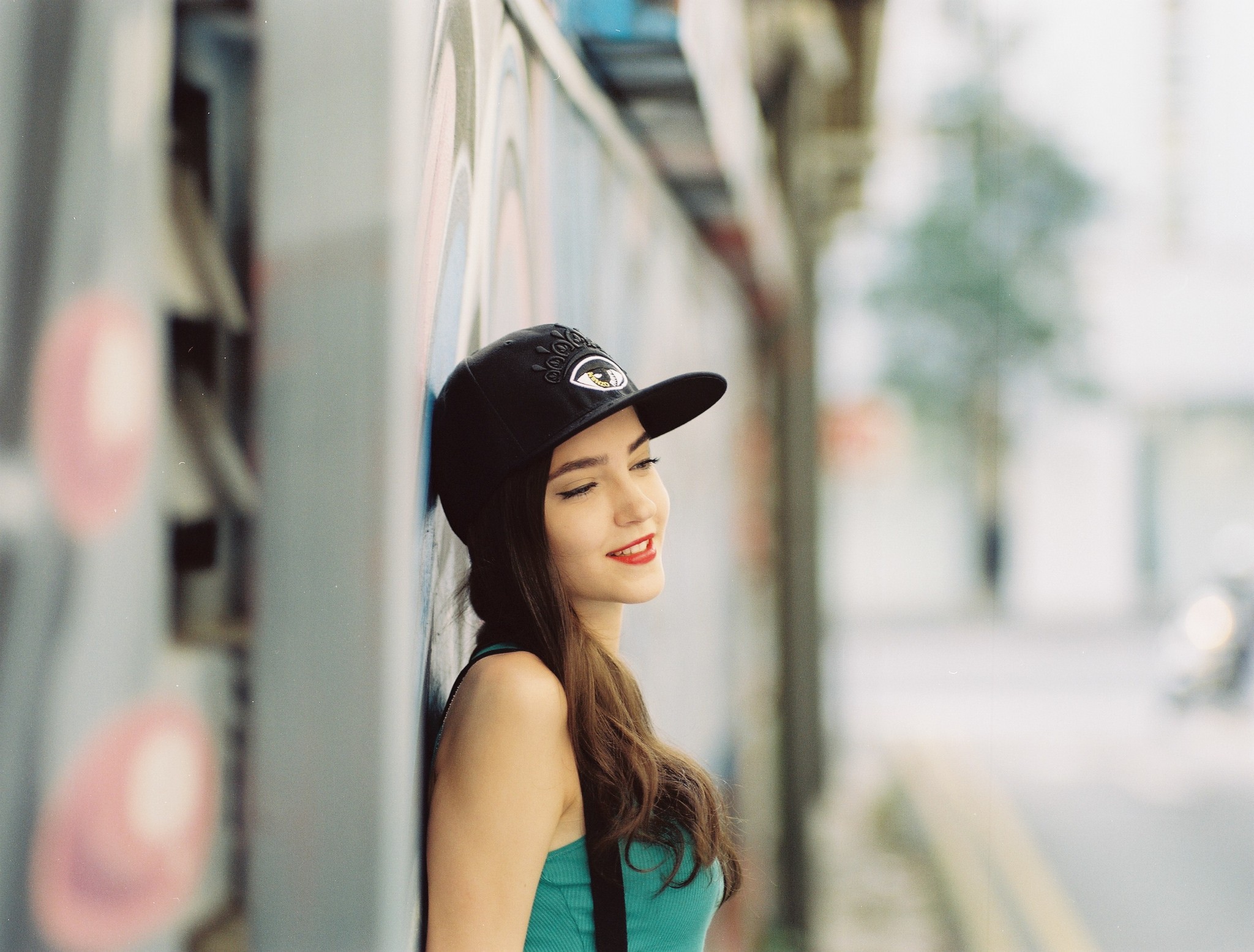 Woman in blue top and black cap leaning against graffiti wall HD Wallpaper