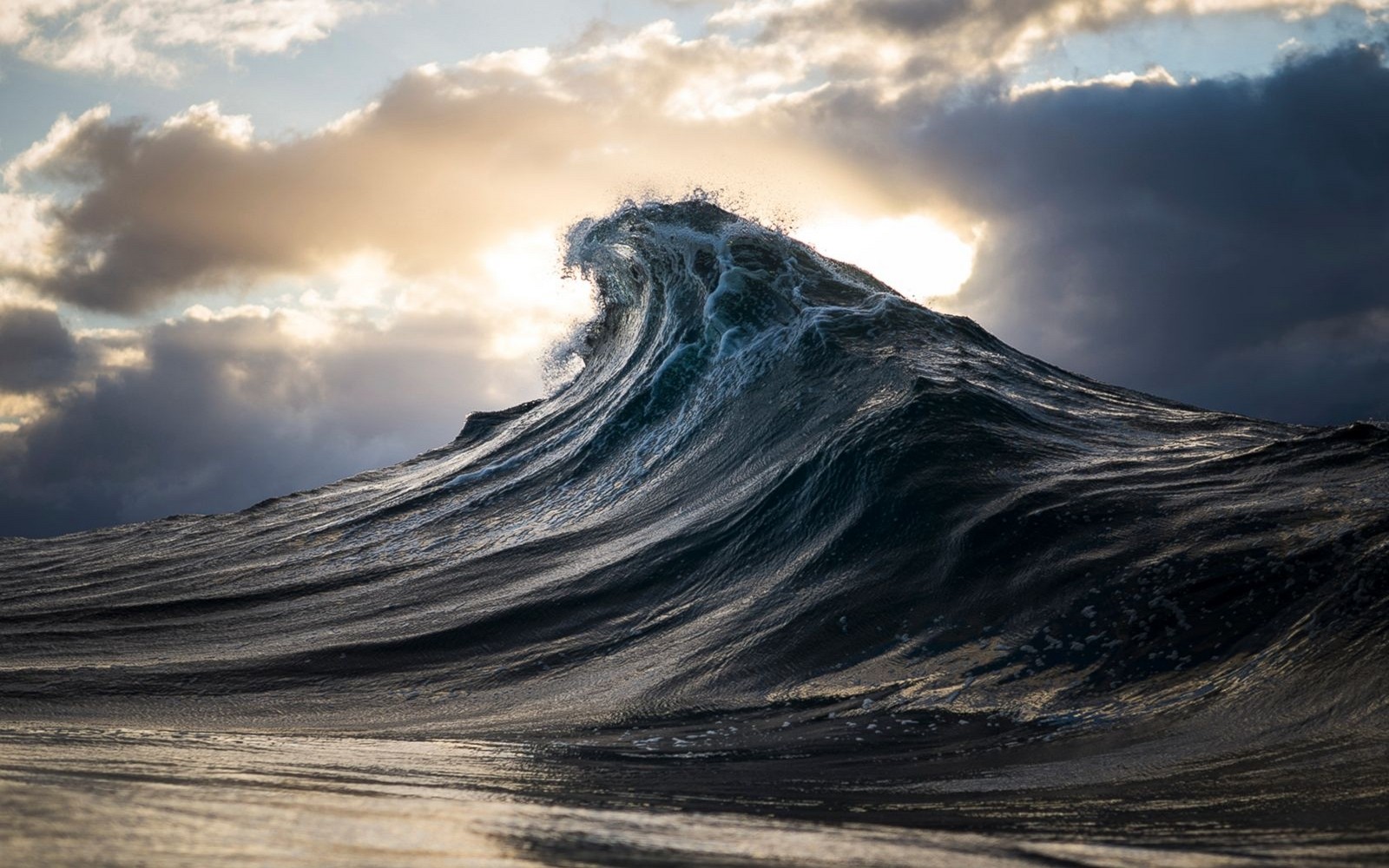 A large wave crashes under dramatic clouds HD Wallpaper