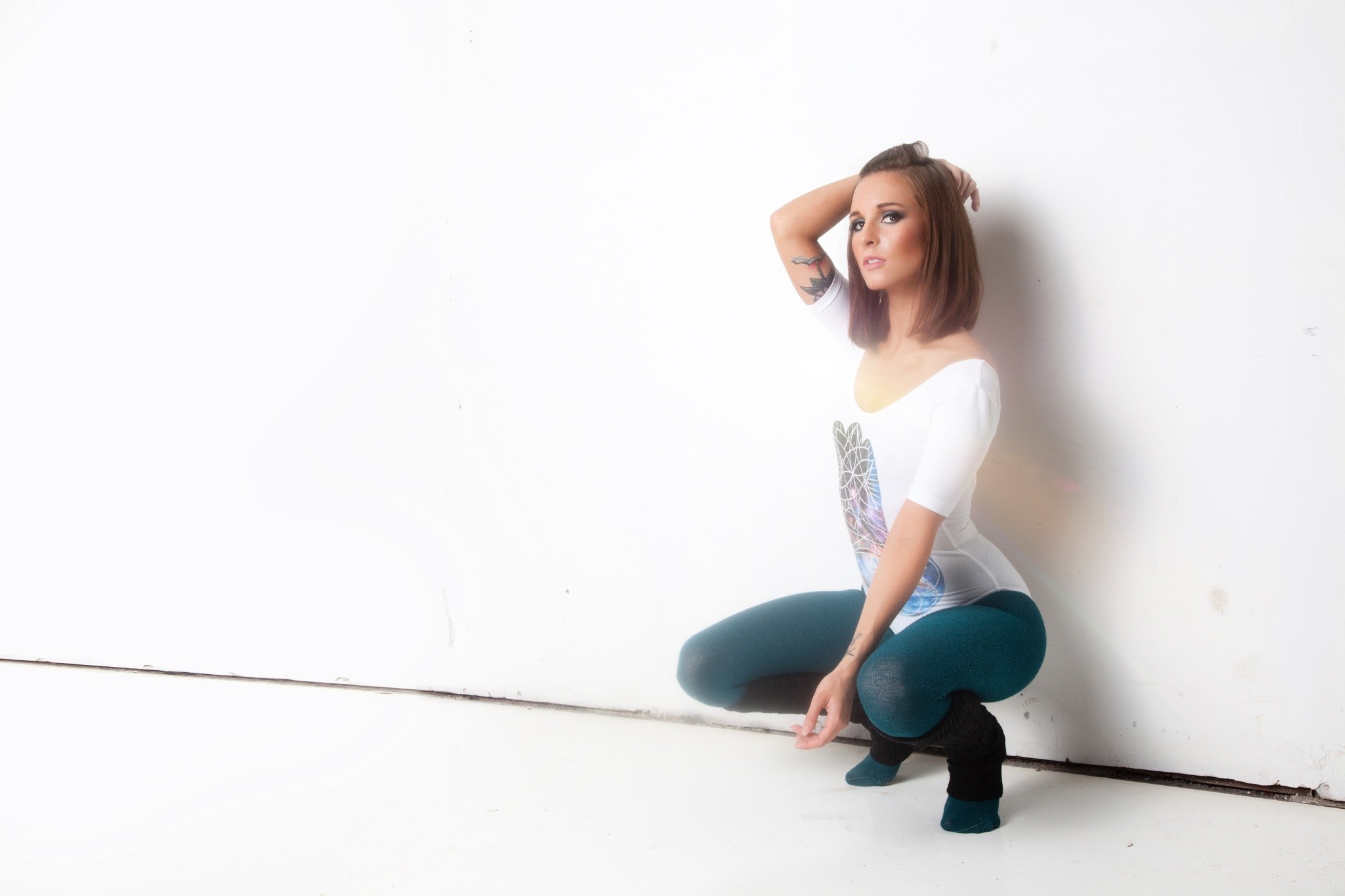 Woman with tattoo kneeling by a white wall HD Wallpaper
