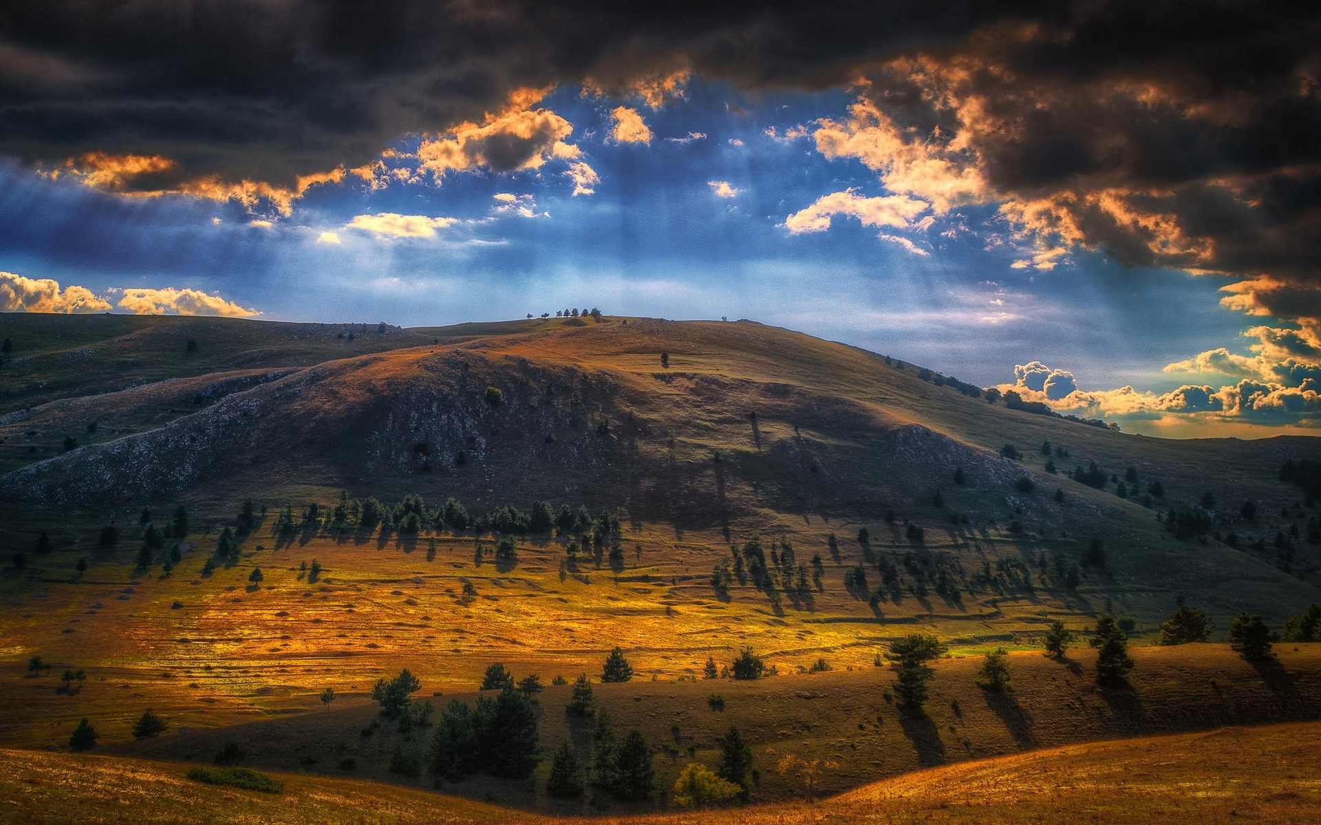 Sun rays breaking through clouds over a mountainous landscape HD Wallpaper