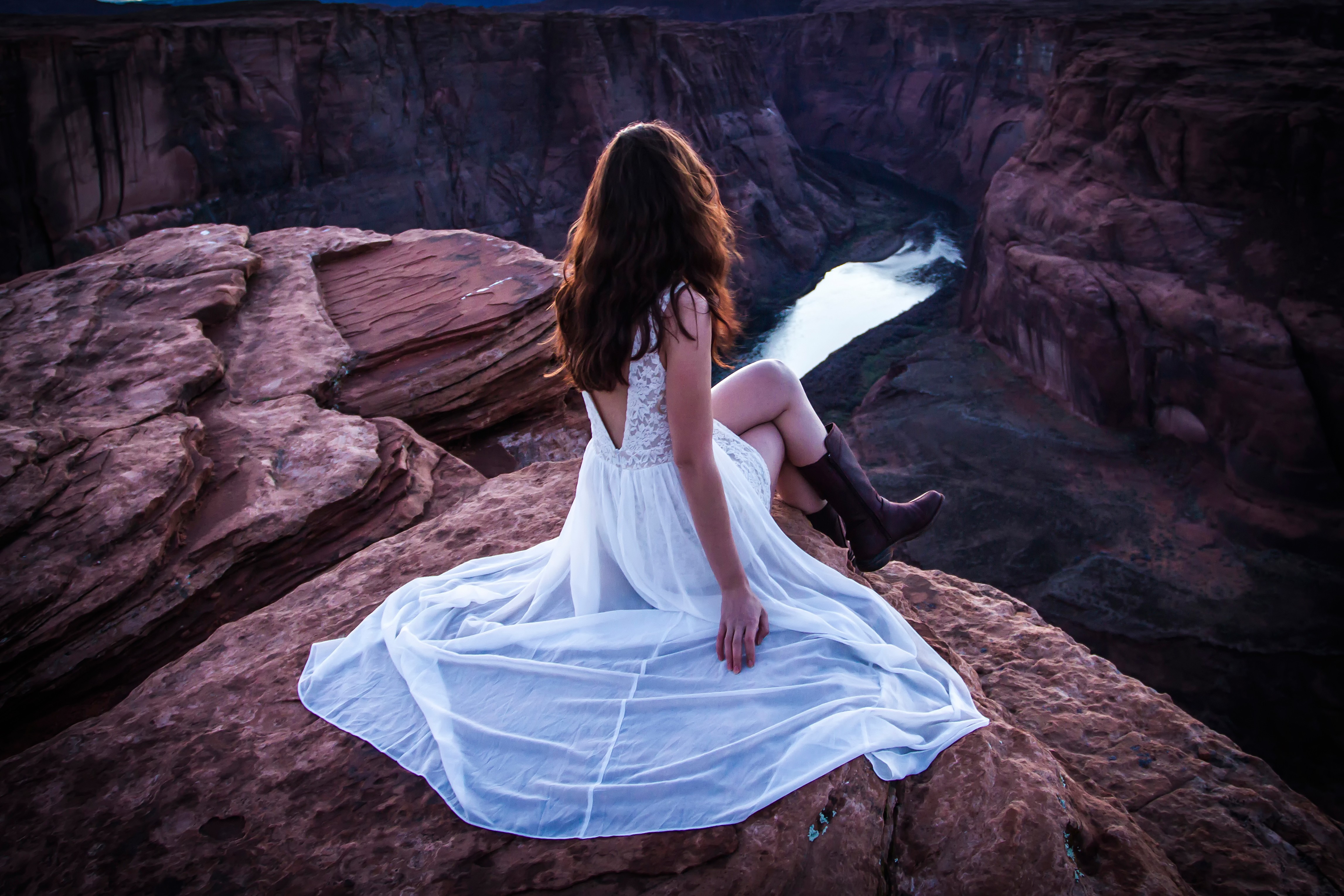 Woman in white dress sitting on cliff edge overlooking canyon HD Wallpaper