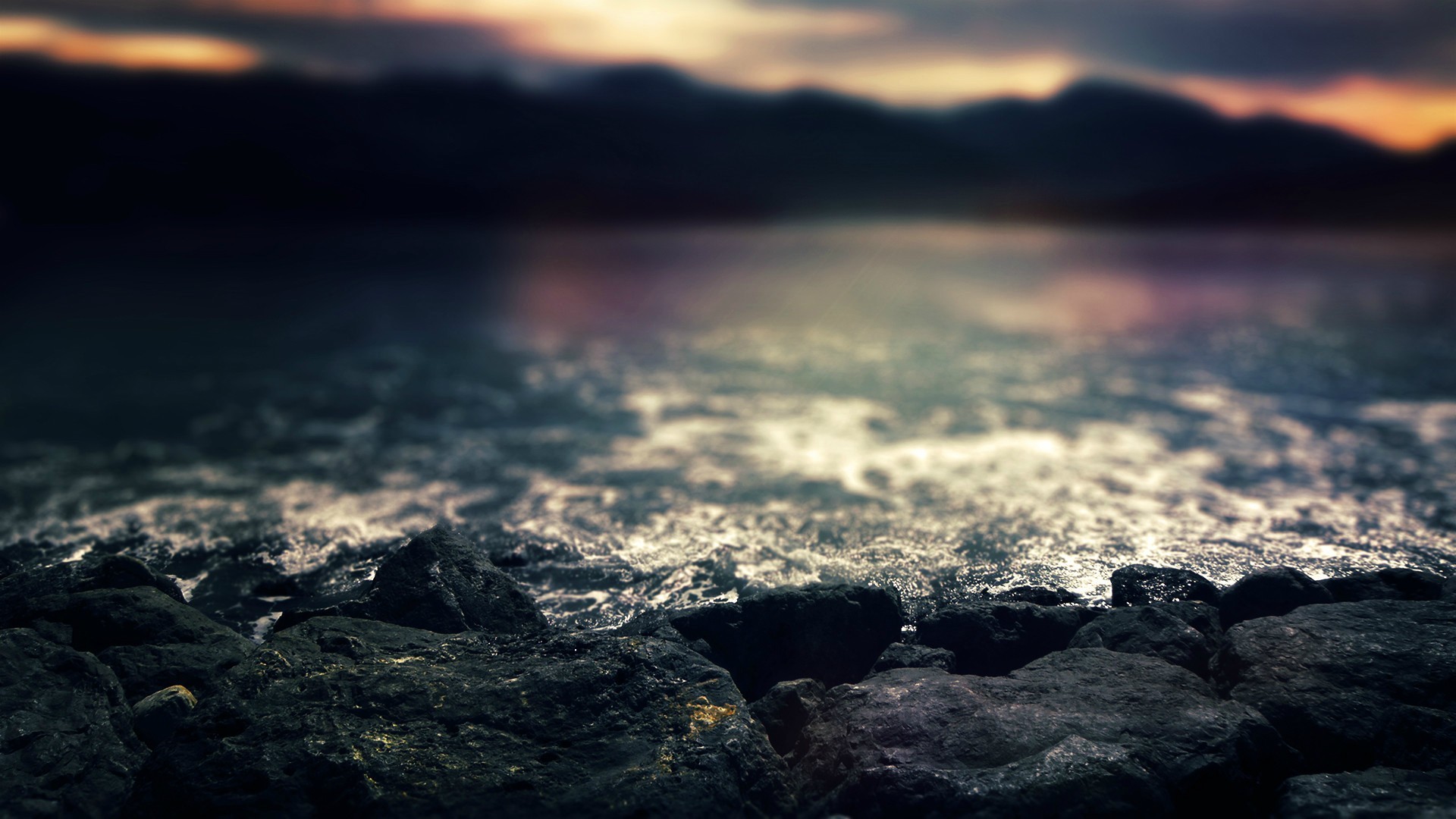 Rocks on the shore with waves and mountains in the background HD Wallpaper