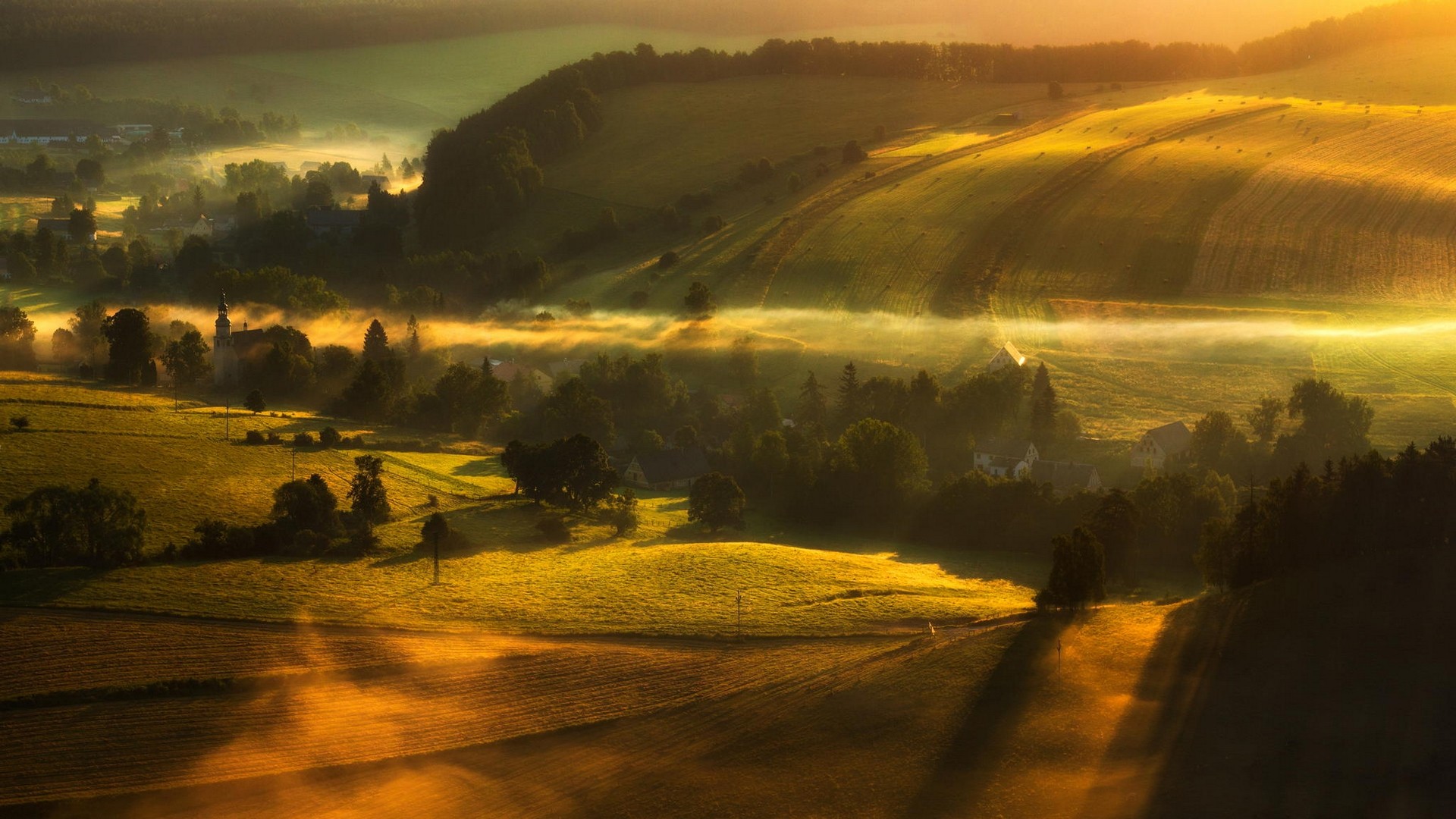 Misty valley with golden sunrise over fields and village HD Wallpaper