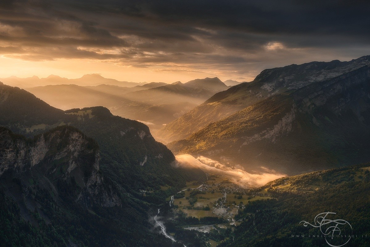 Sunlight streams through a mountain valley with a village HD Wallpaper