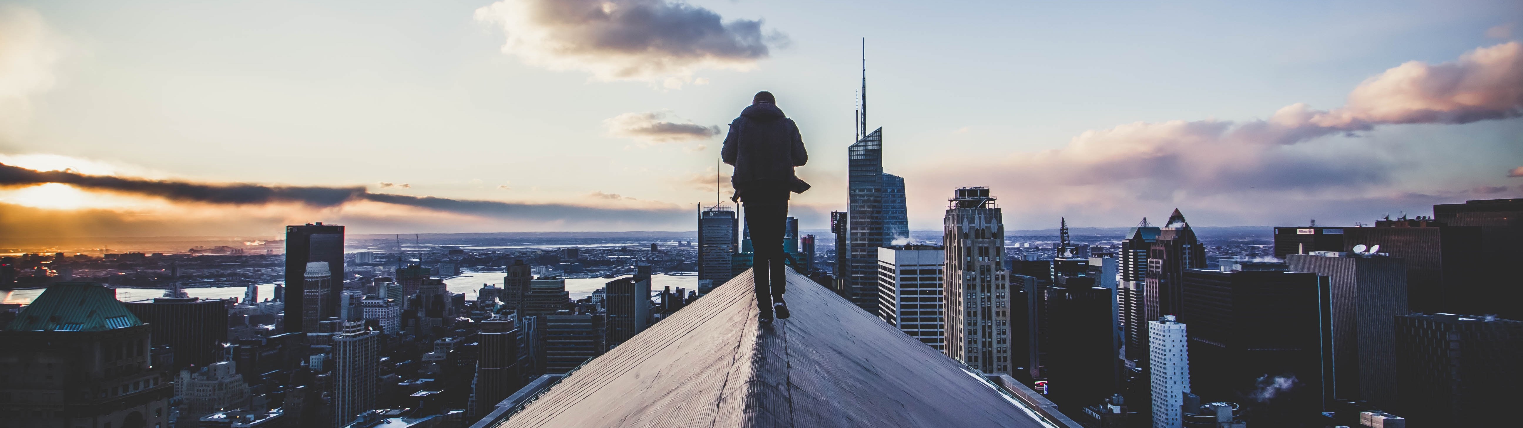 Man walks on a rooftop overlooking a cityscape at sunset HD Wallpaper