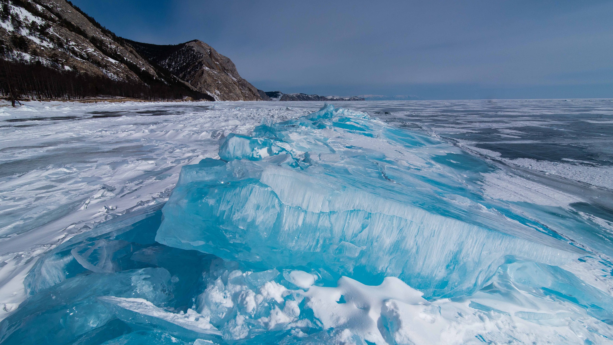 Blue ice formations on a frozen lake with mountains HD Wallpaper