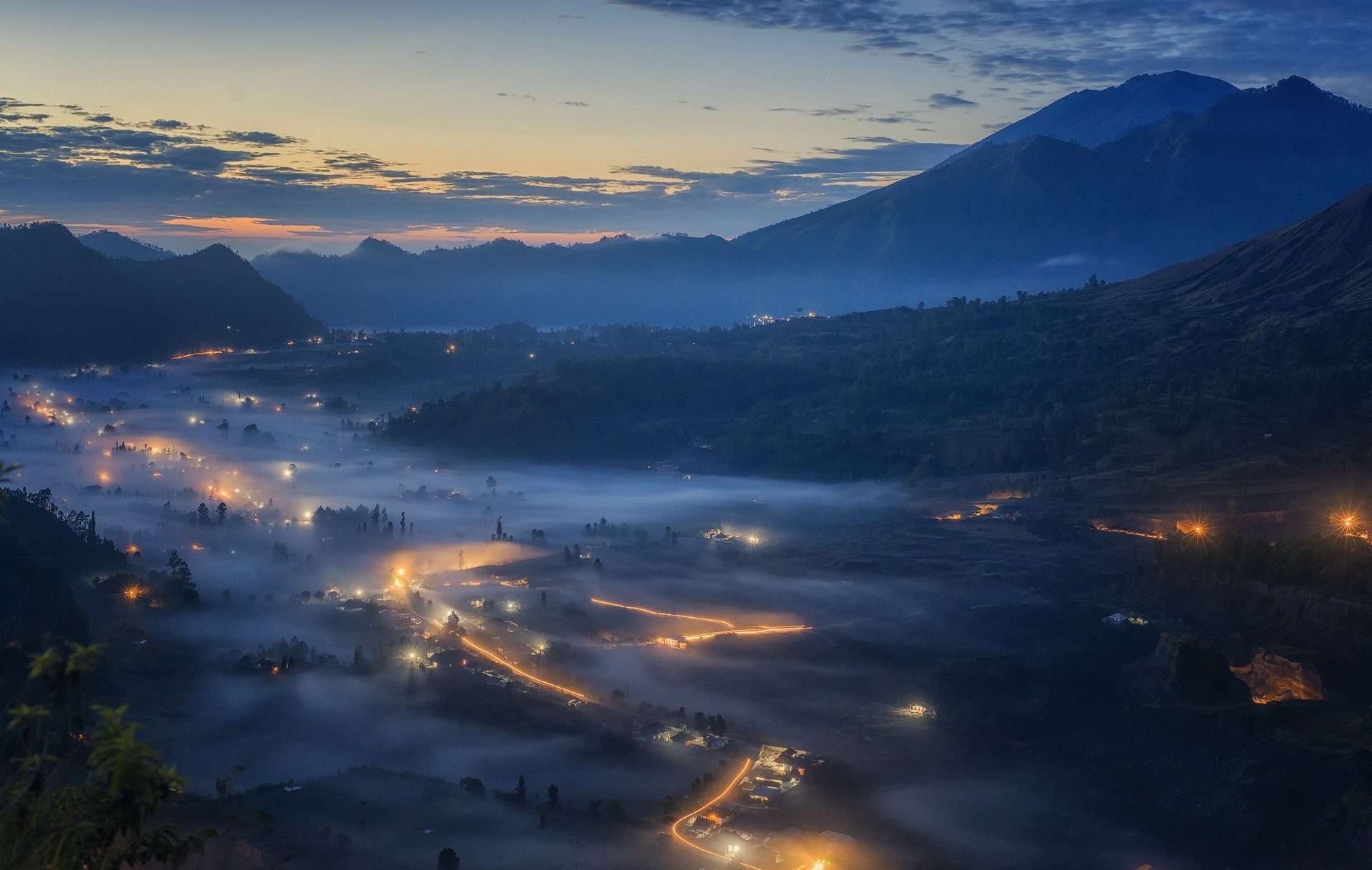 Misty valley with mountains and village lights at dawn HD Wallpaper